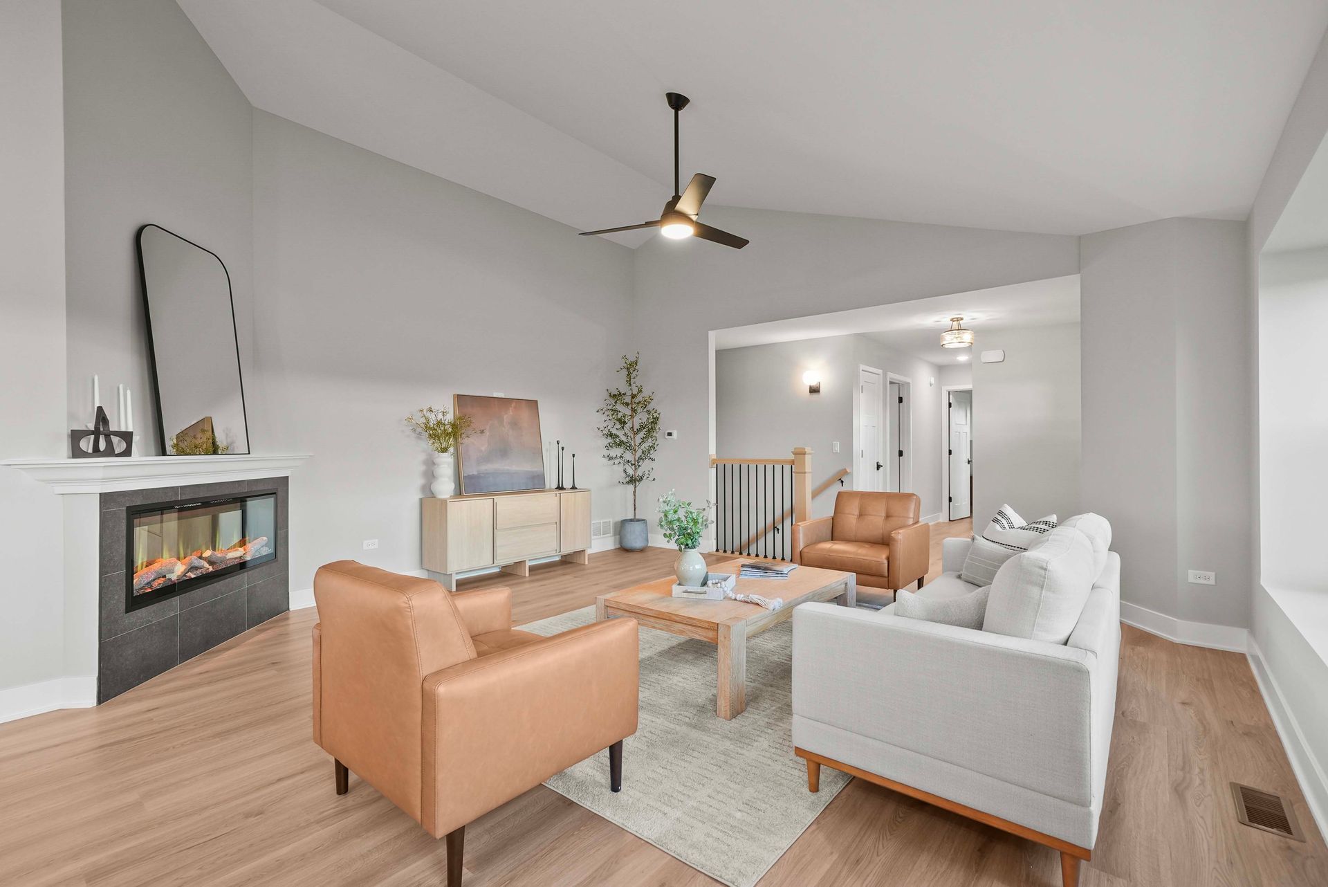 Bright modern living room with white sofa, tan chairs, fireplace, and ceiling fan
