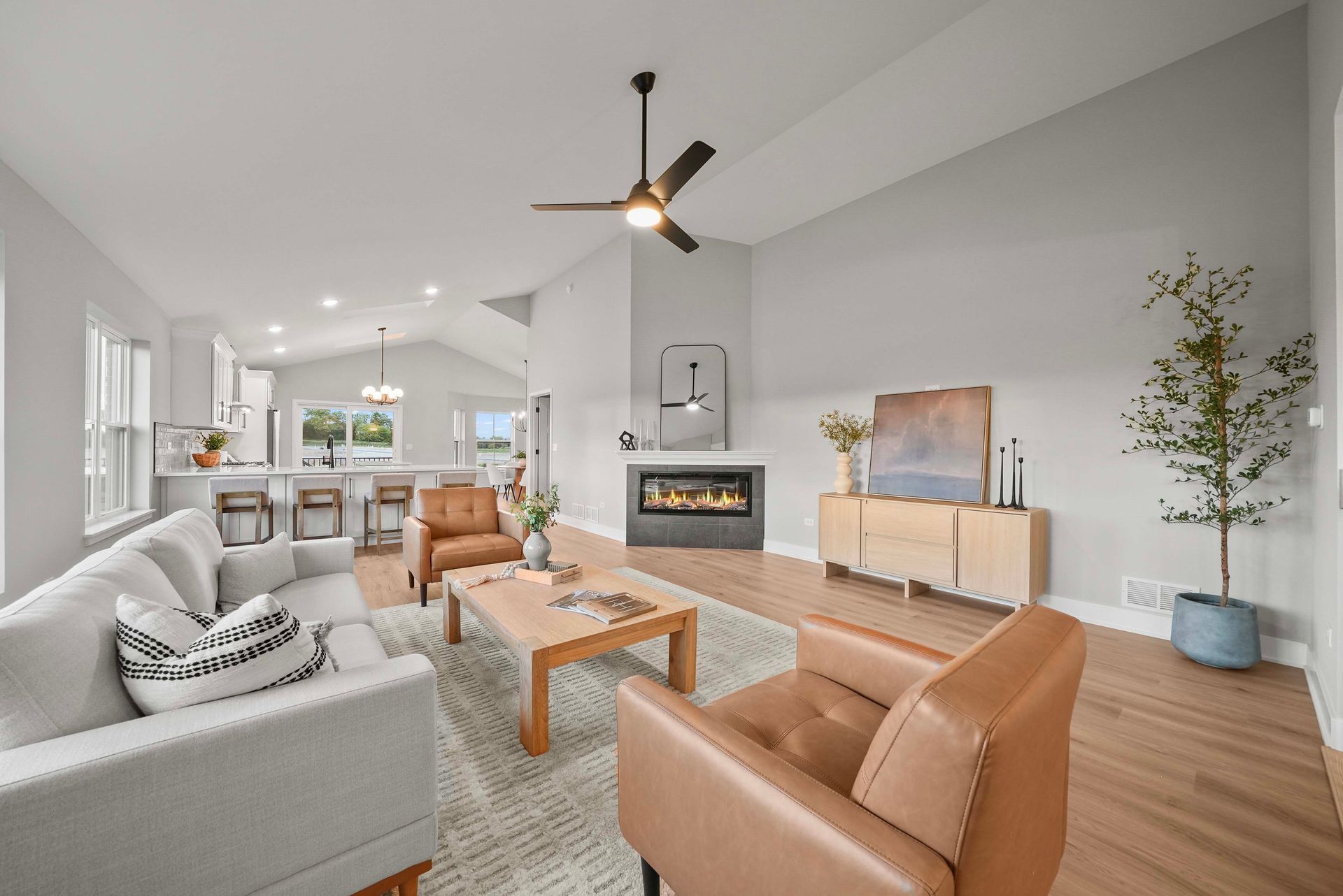 Bright modern open-plan living room with white and tan seating, fireplace, TV, and kitchen beyond