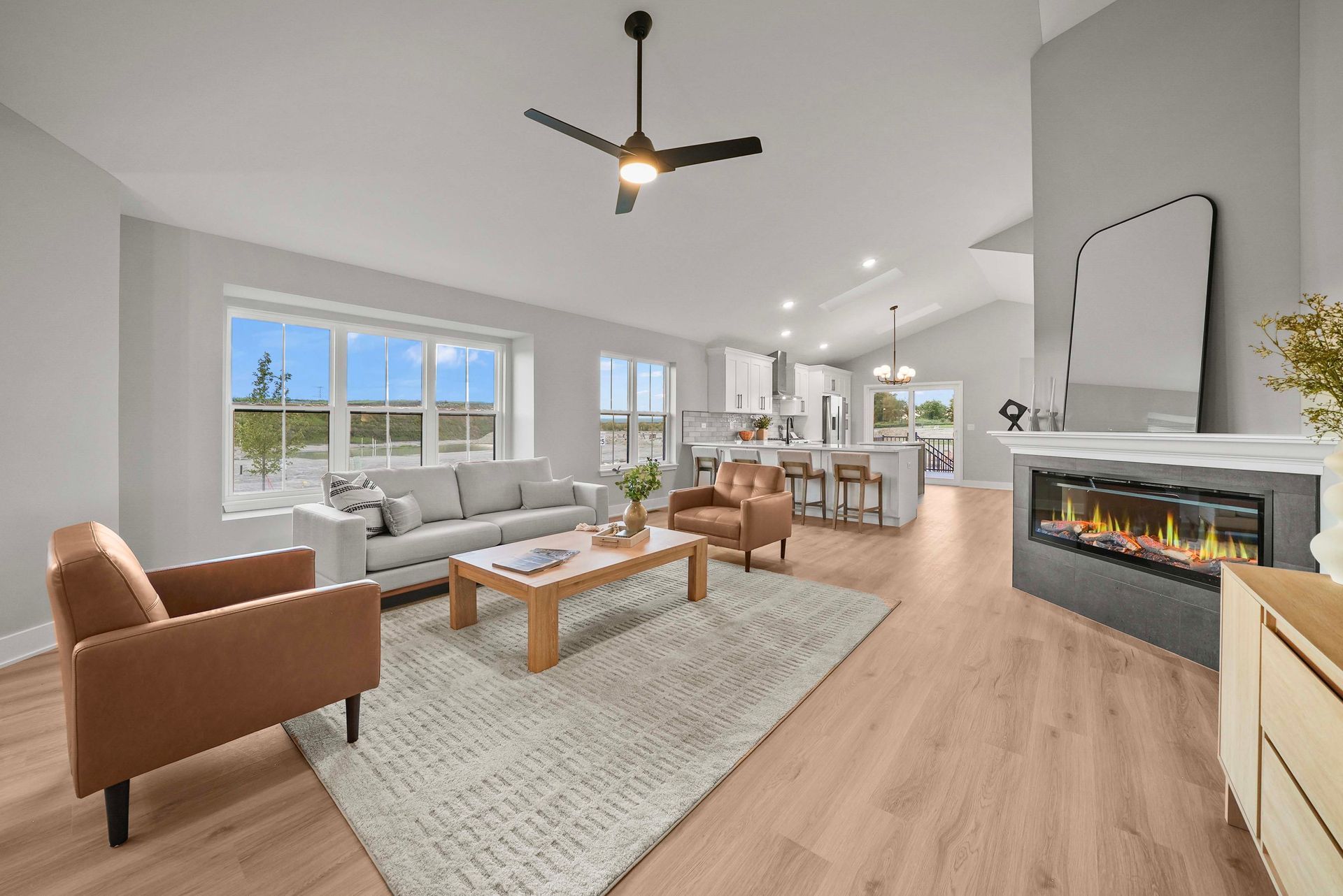 Bright modern living room with white sectional, tan chair, fireplace, wood floors, and open kitchen in the background