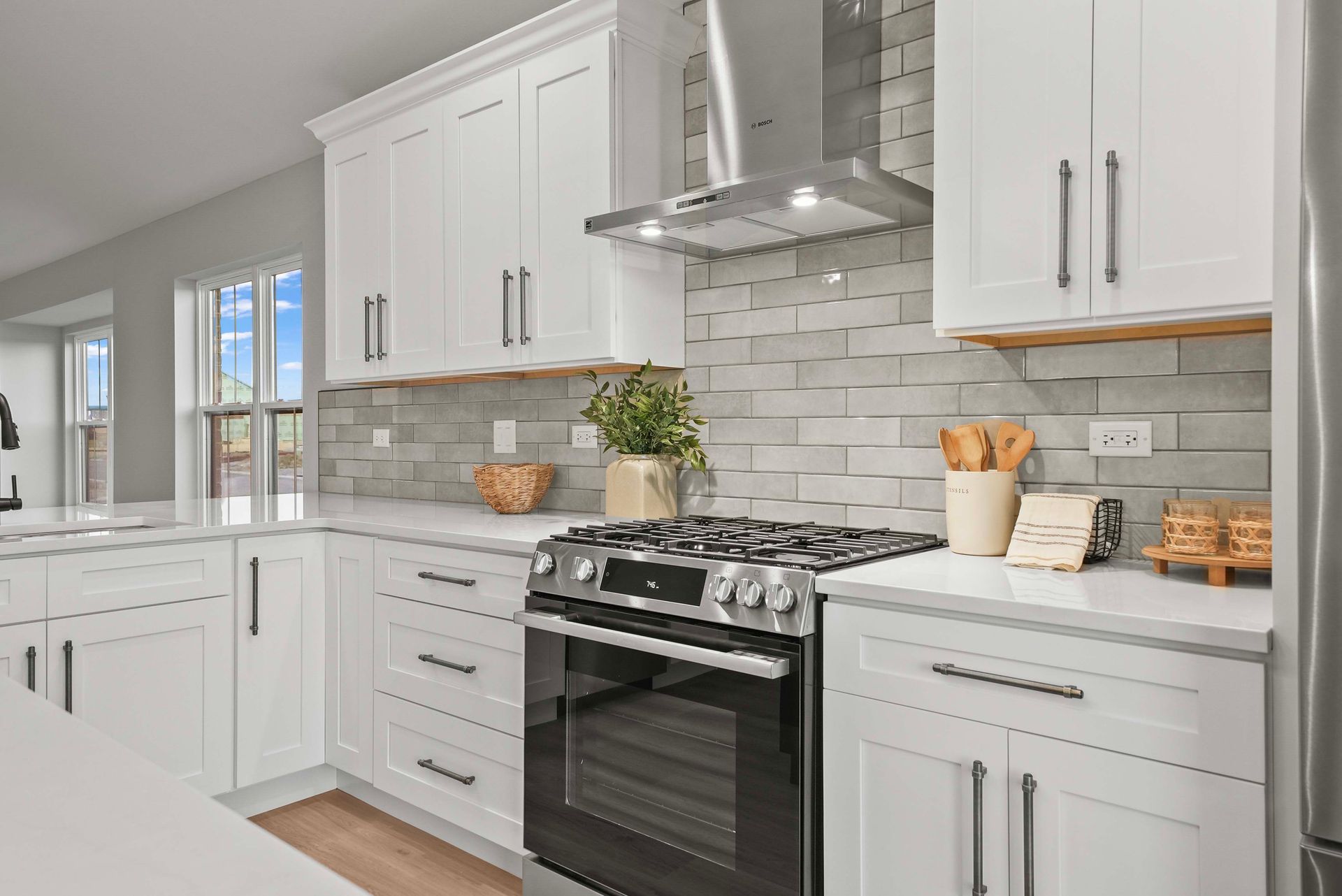 Bright modern kitchen with white cabinets, stainless stove, and gray tile backsplash