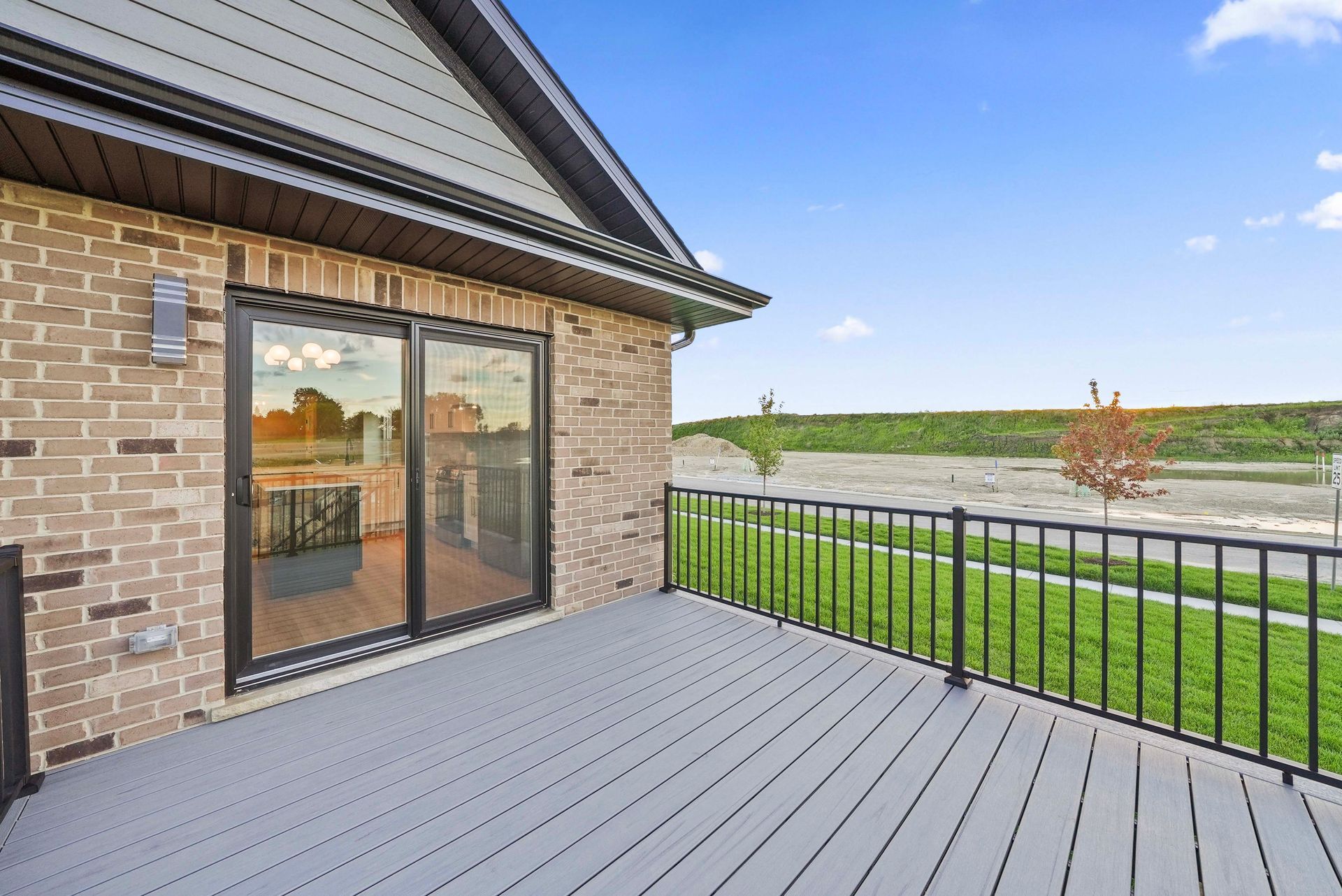 Modern brick home patio with gray decking, black railing, and sliding glass doors overlooking a grassy field