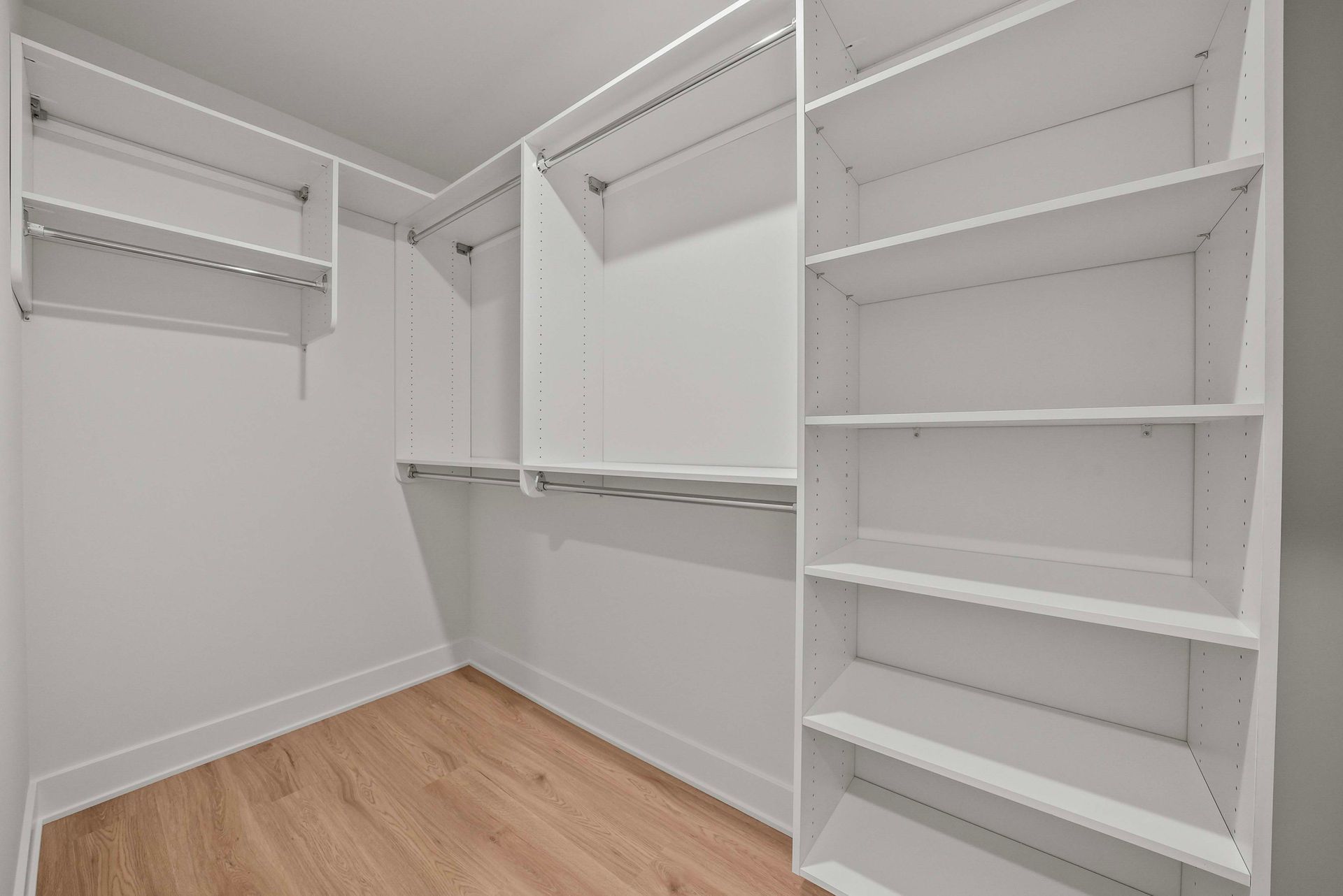 Empty white walk-in closet with built-in shelves and hanging rods, light wood floor.