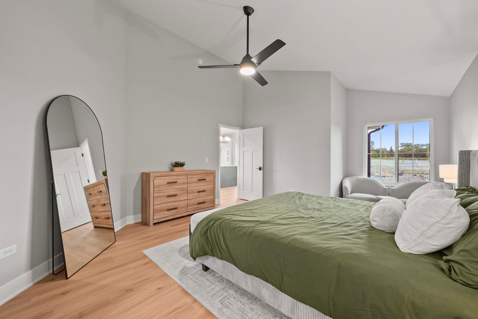 Bright bedroom with green bedspread, dresser, mirror, ceiling fan, and window view.
