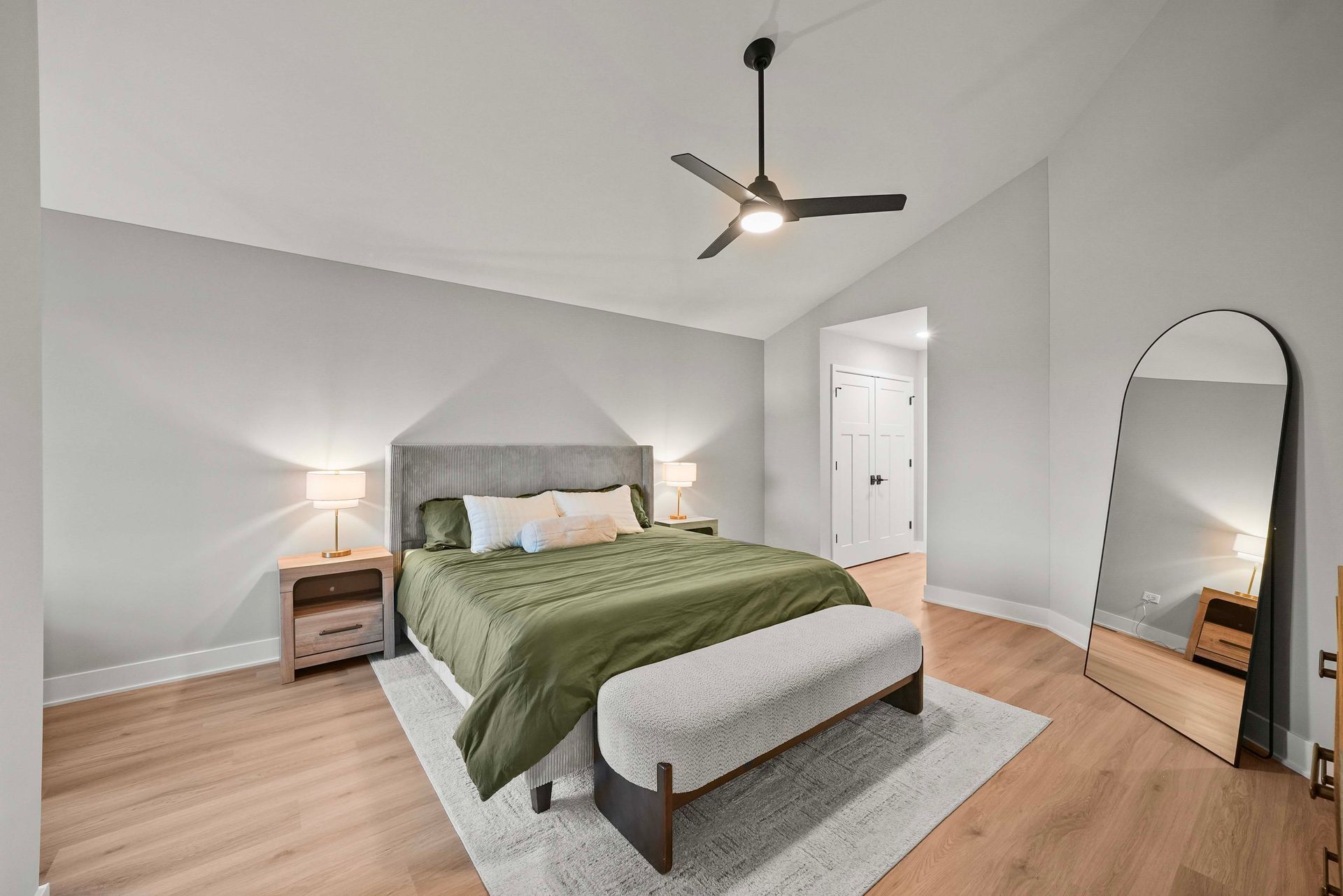 Bright bedroom with a gray bed, green bedding, wood floors, and a standing mirror.