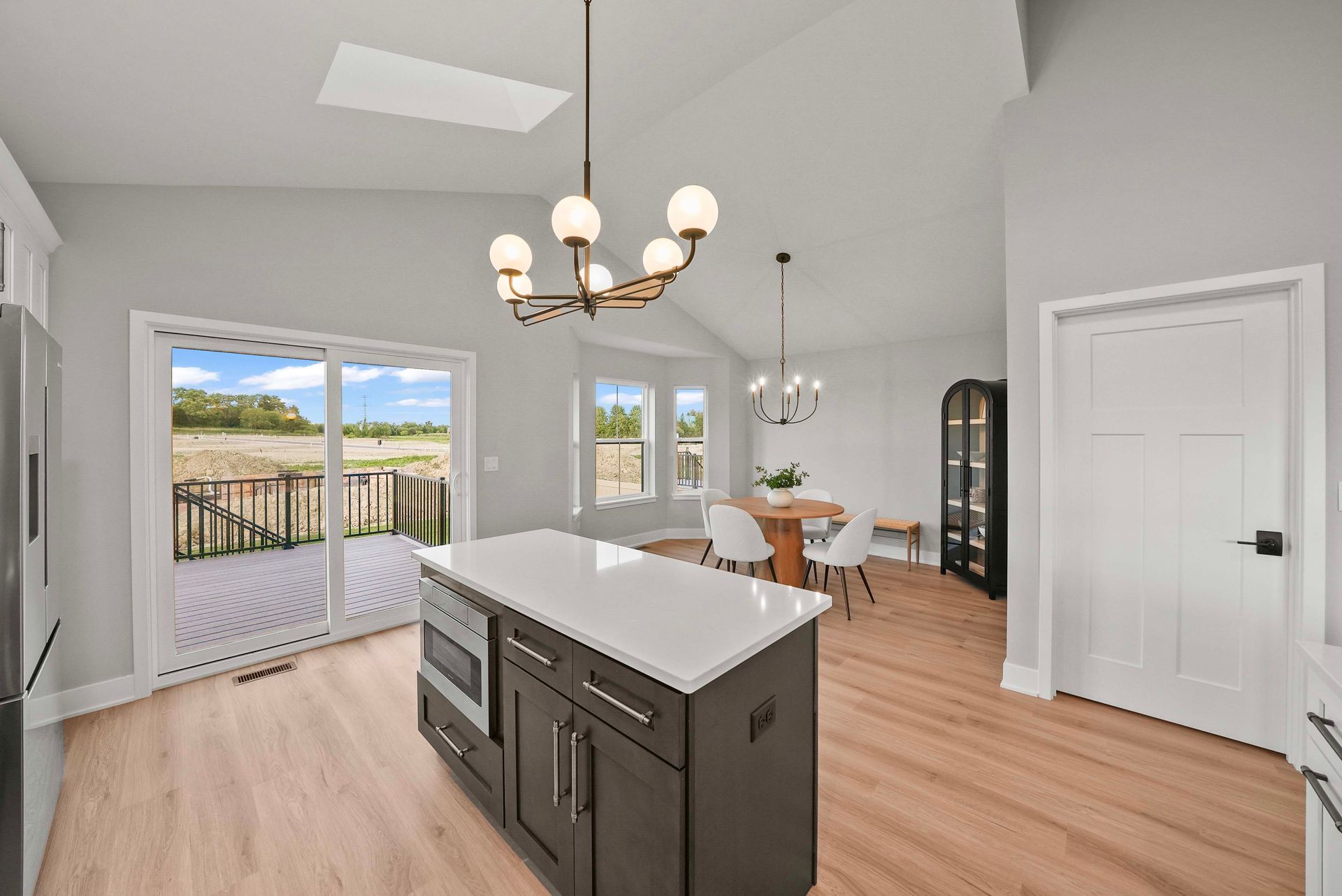 Bright open kitchen with island, white cabinets, wood floors, chandelier, and sliding doors to a deck.