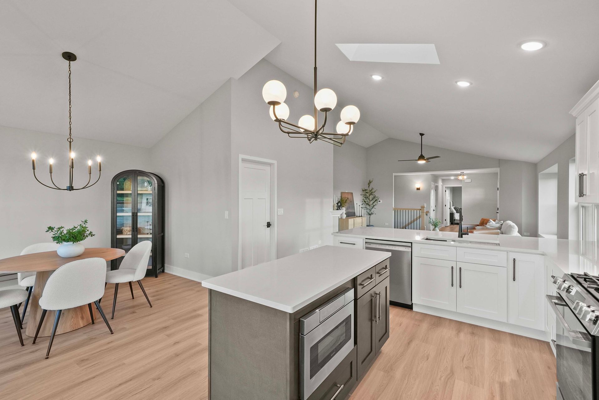 Bright open-concept kitchen and dining area with white cabinets, wood floors, and modern chandeliers