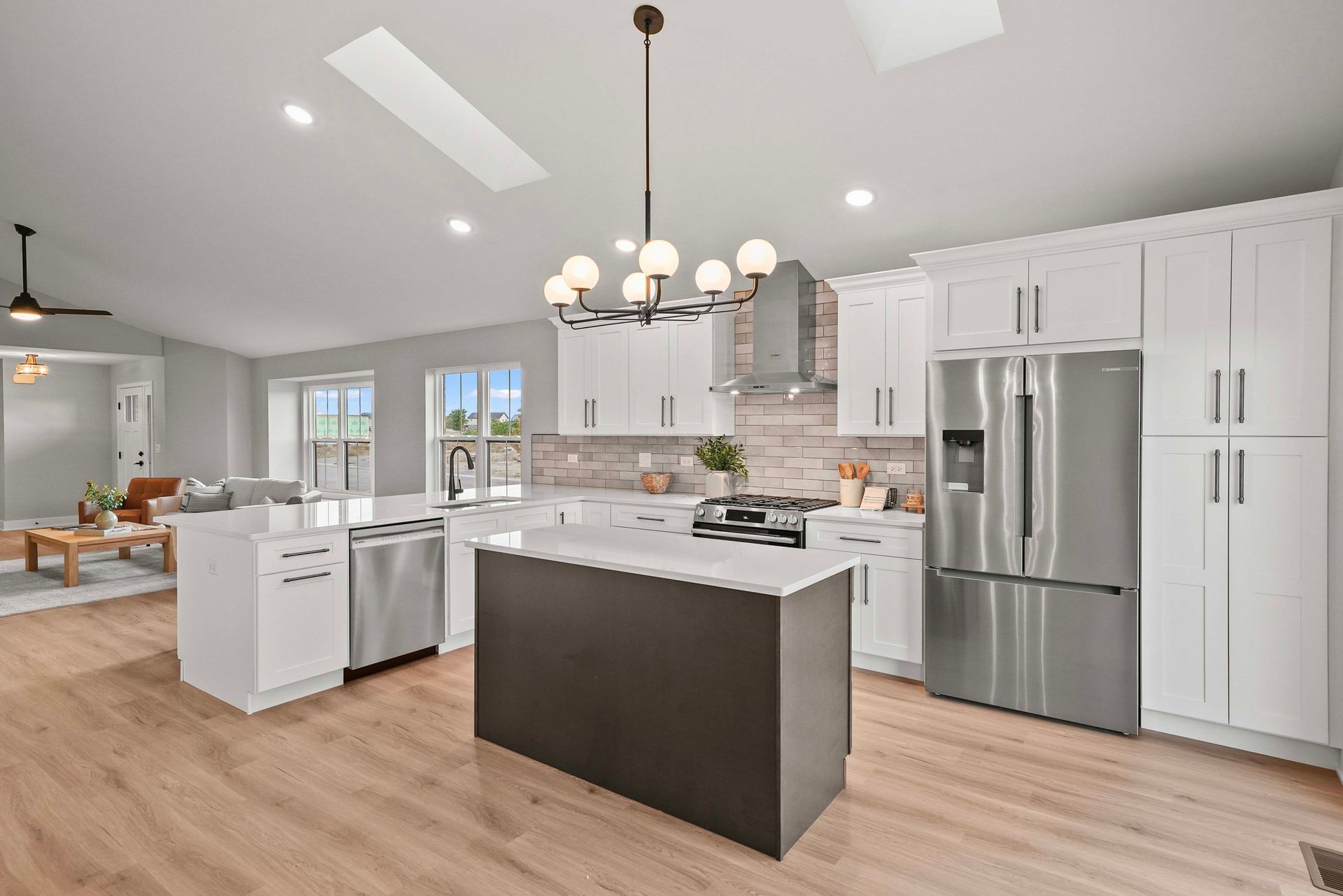 Bright modern kitchen with white cabinets, stainless steel appliances, and a dark island with pendant lights.
