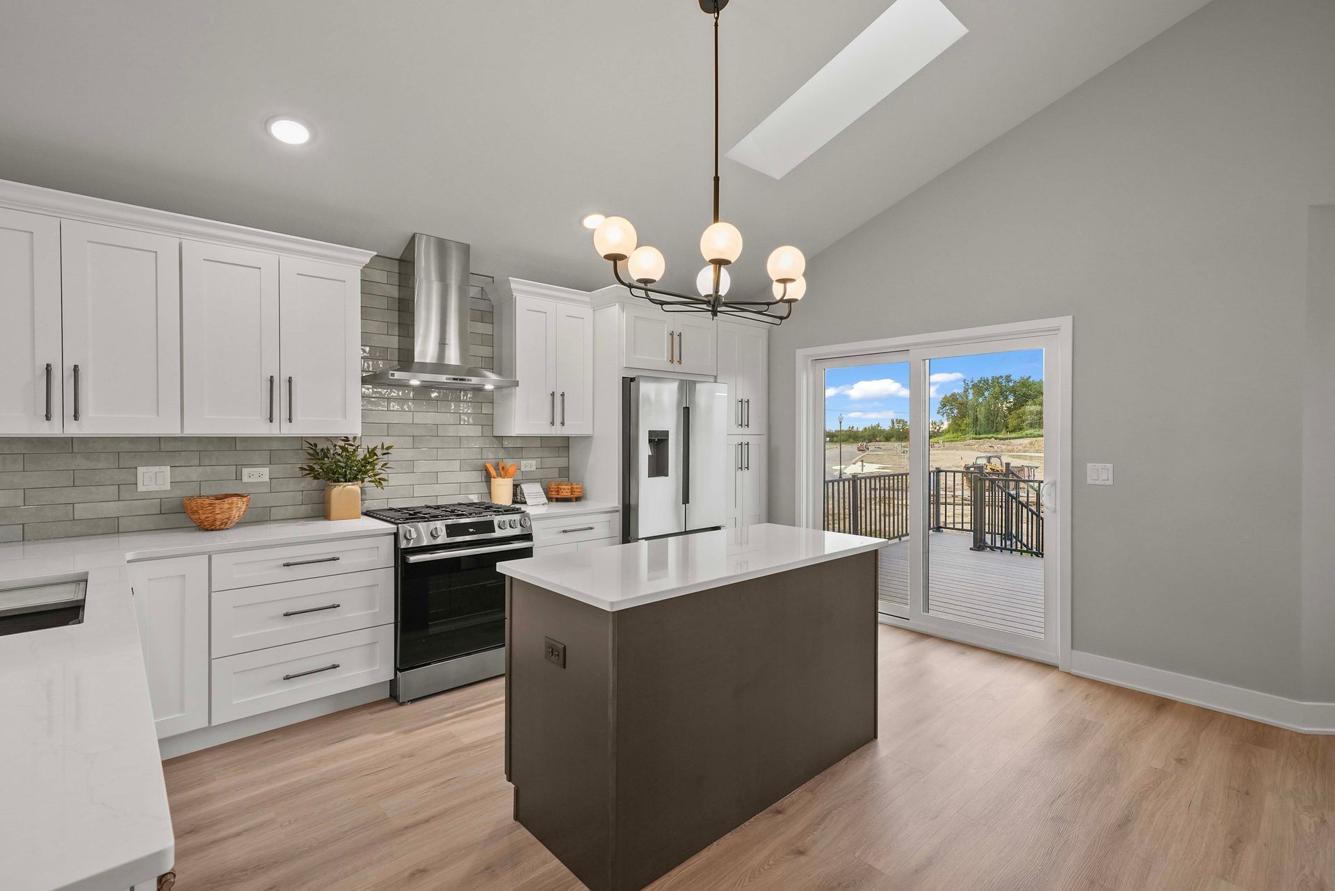 Bright modern kitchen with white cabinets, central island, chandelier, and glass doors to a deck.