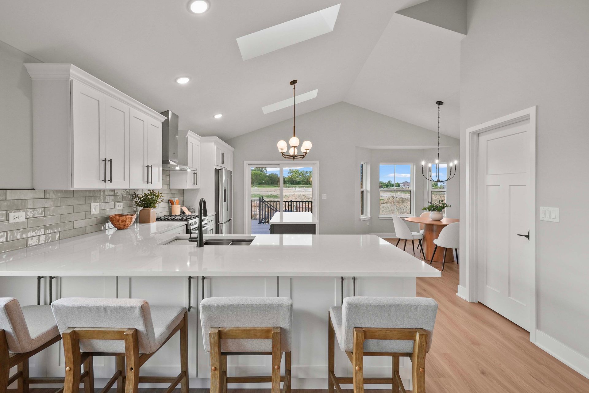 Bright modern white kitchen with island, barstools, pendant lights, and open view to dining area and patio.