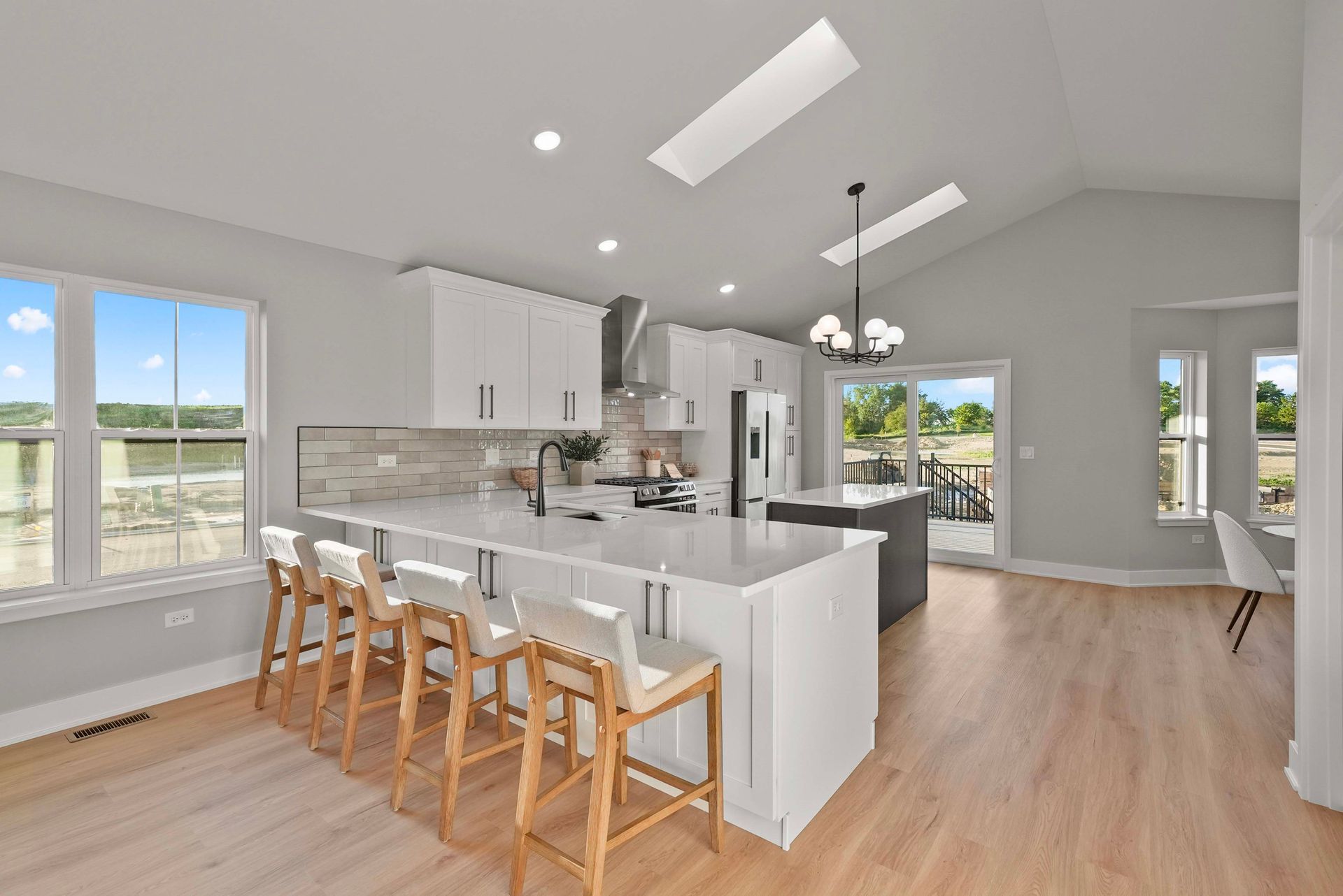 Bright open kitchen with white cabinets, island seating, wood floors, and large windows