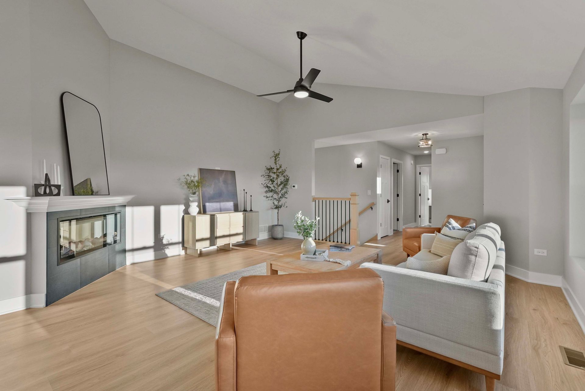 Bright modern living room with tan and gray seating, fireplace, ceiling fan, and hardwood floors