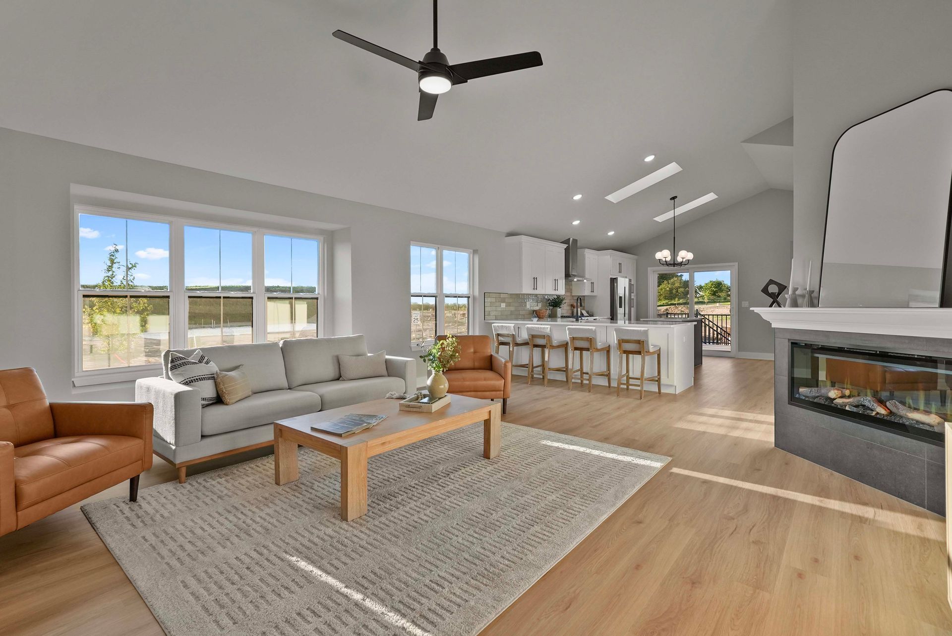 Modern open-plan living room with gray sofas, wood coffee table, fireplace, and kitchen island.