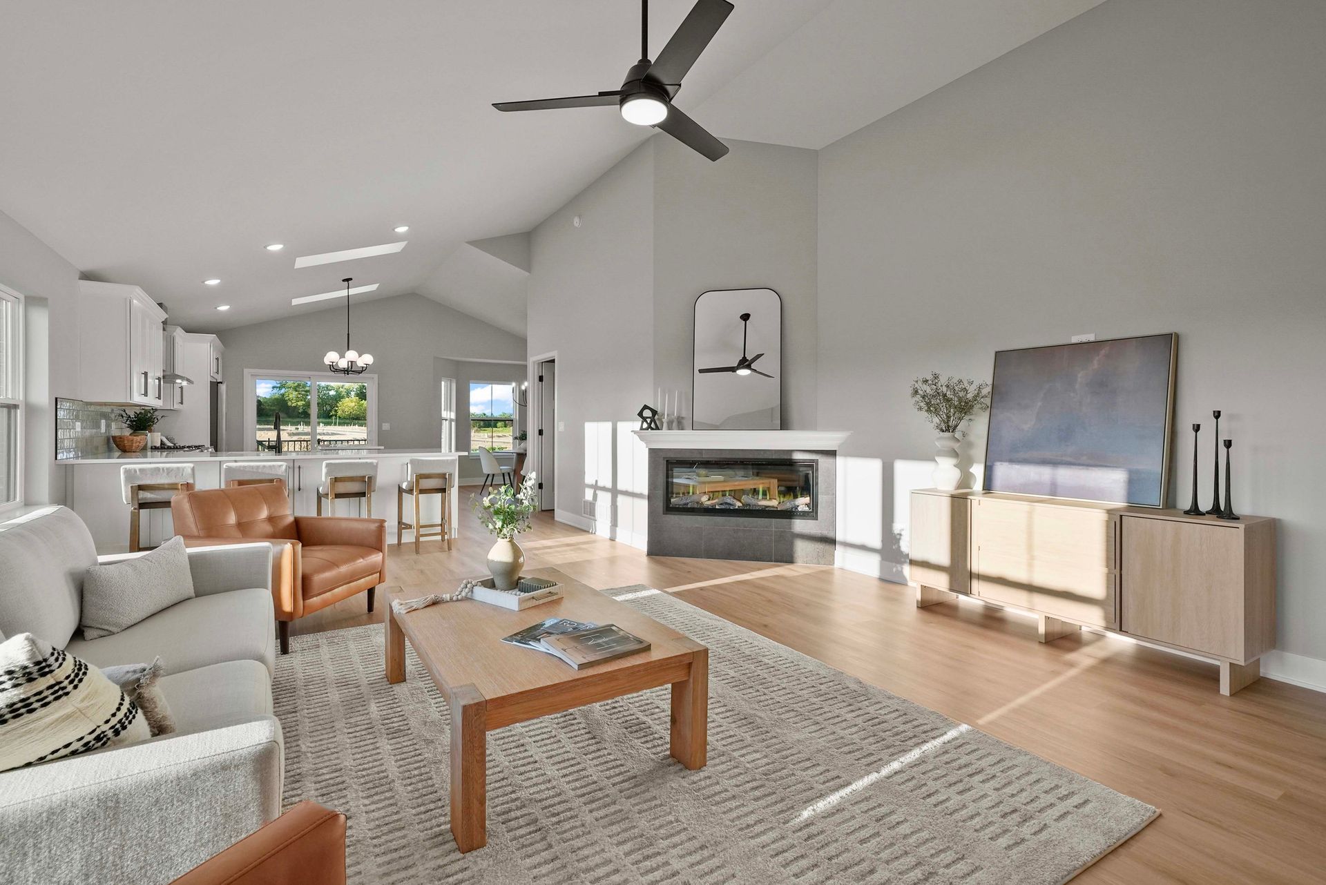 Bright modern living room with gray sofa, fireplace, wood coffee table, and ceiling fan under vaulted ceiling