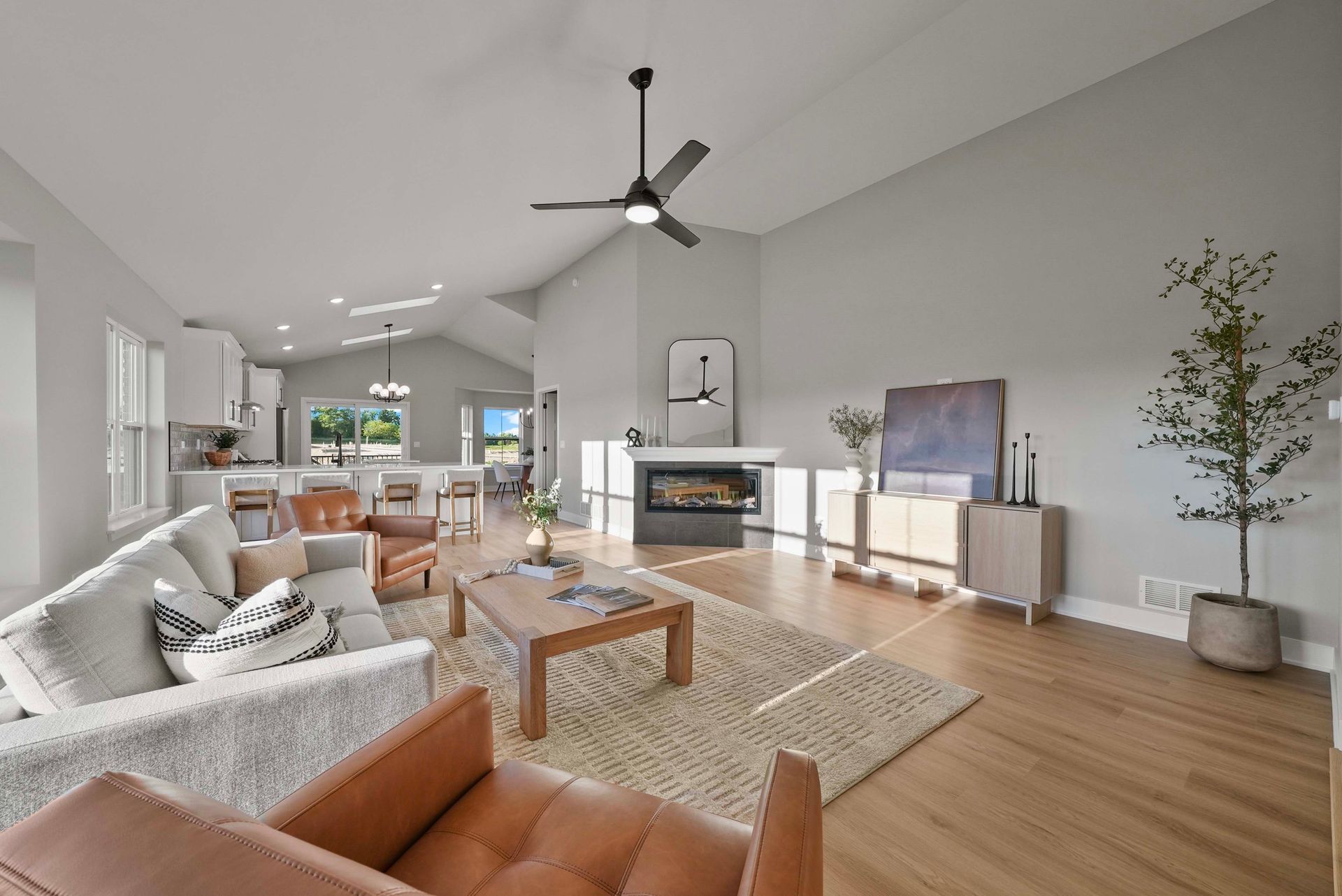 Bright open living room with white sofas, wood floors, fireplace, ceiling fan, and large windows