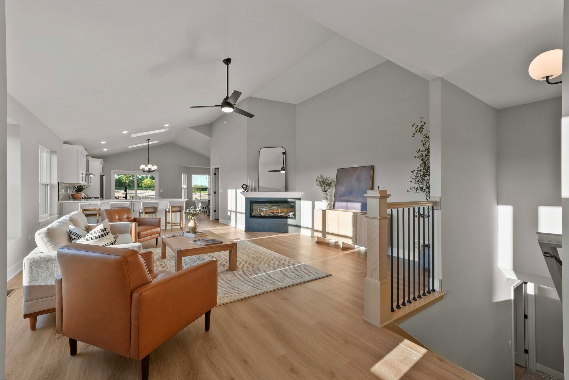 Modern open-concept living room with tan chairs, fireplace, ceiling fan, and light wood floors