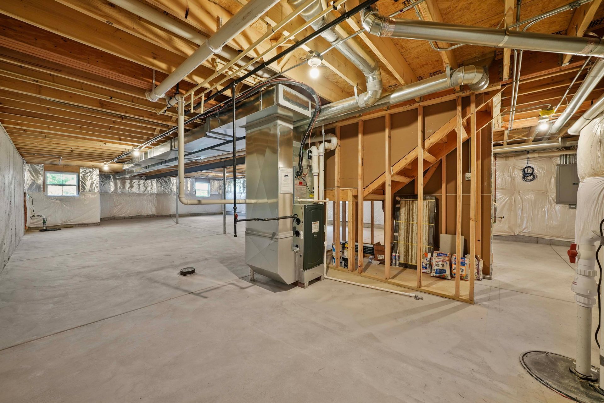 Unfinished basement with exposed beams, concrete floor, HVAC unit, and framed walls.
