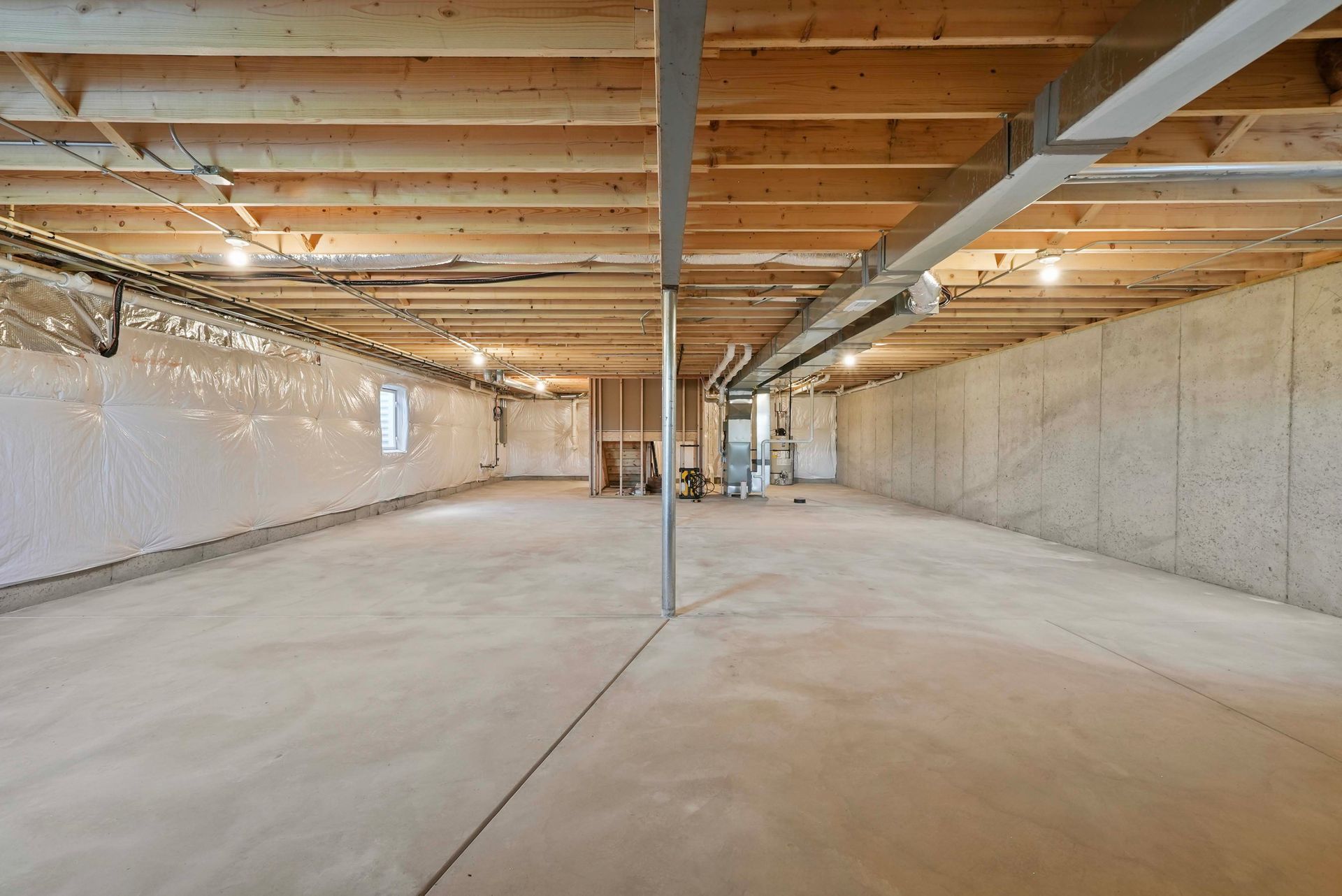 Empty unfinished basement with concrete floor, exposed beams, and ductwork.