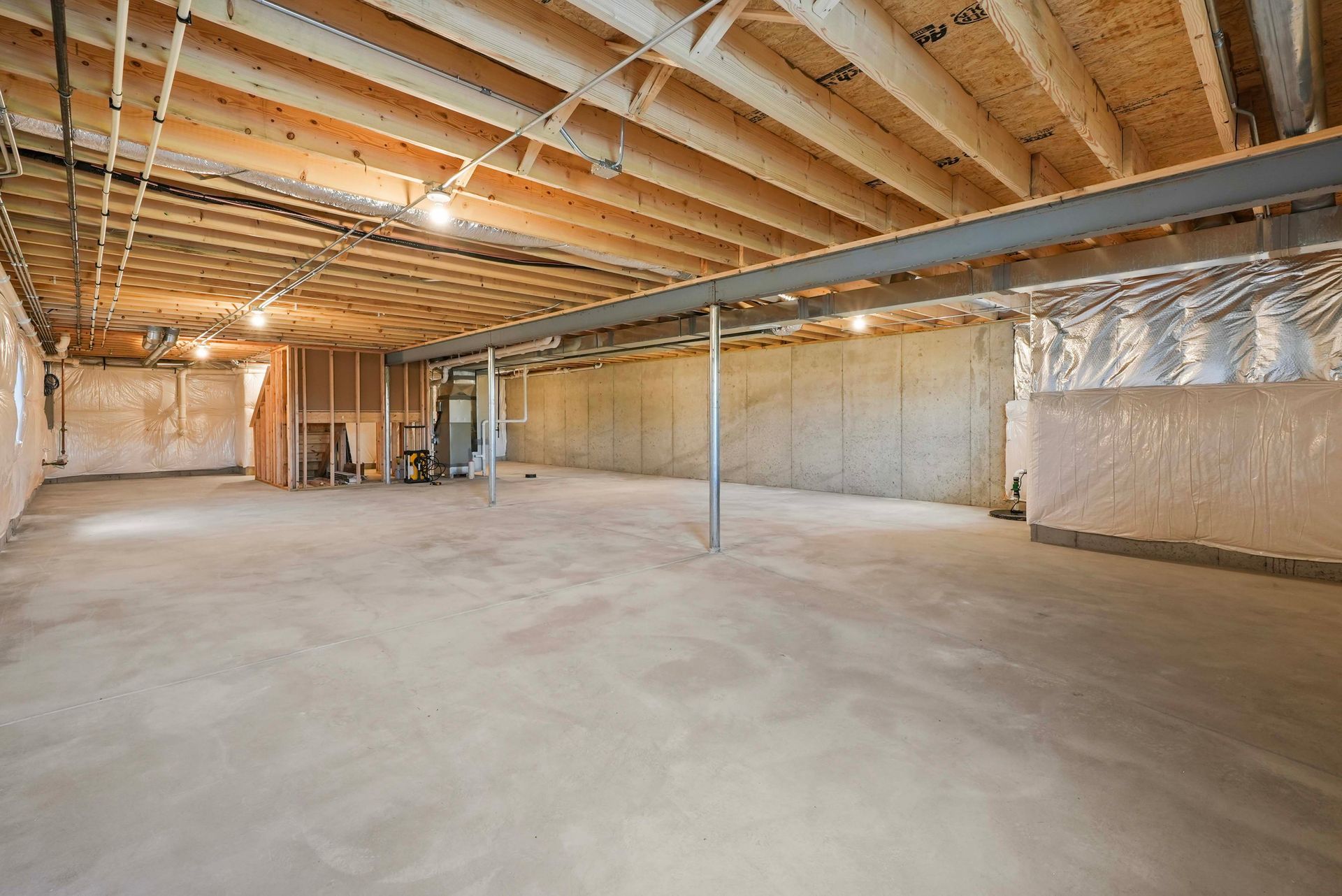 Unfinished basement interior with exposed beams, insulation, and concrete floor