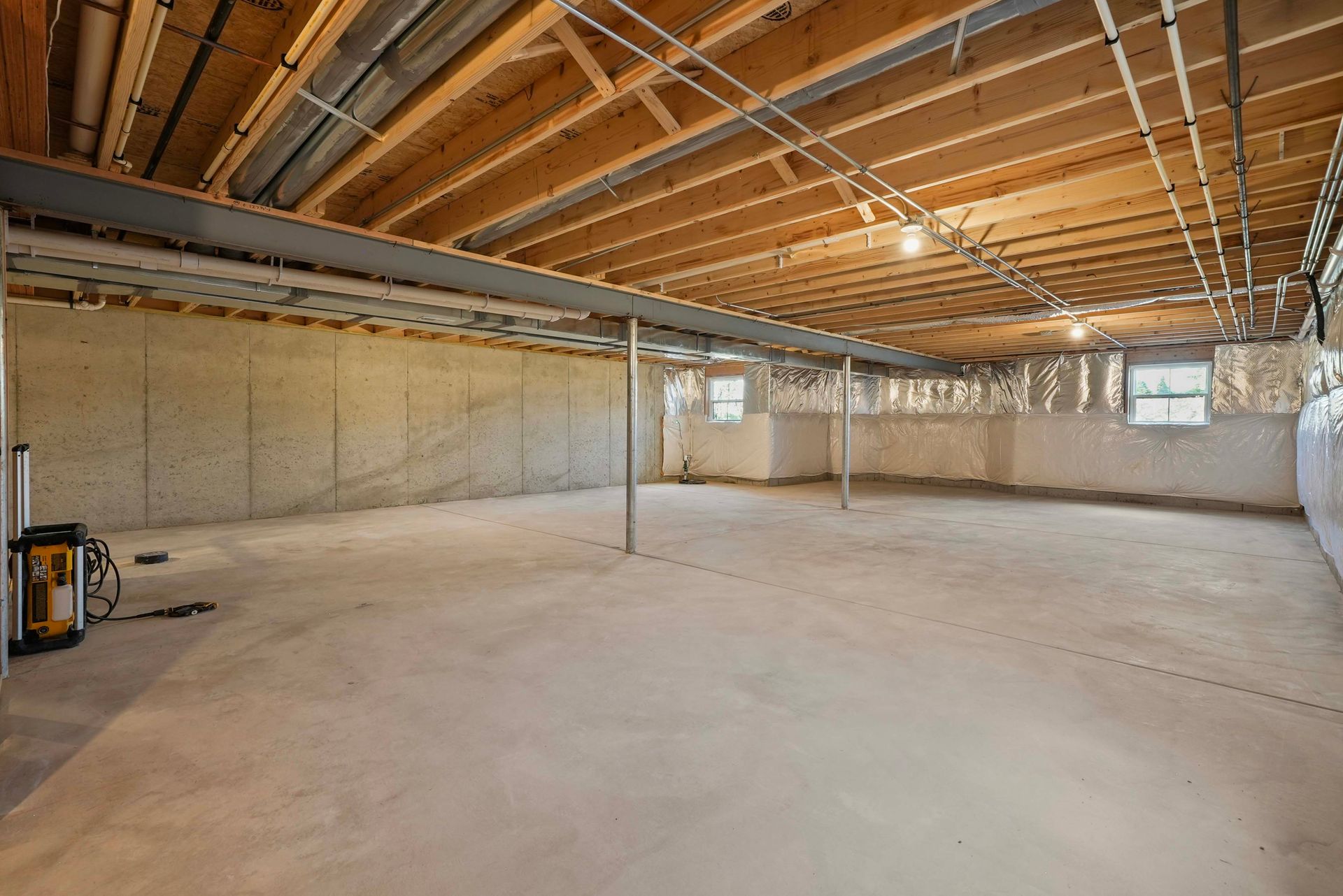 Empty unfinished basement with exposed wood beams, concrete floor, and unfinished walls