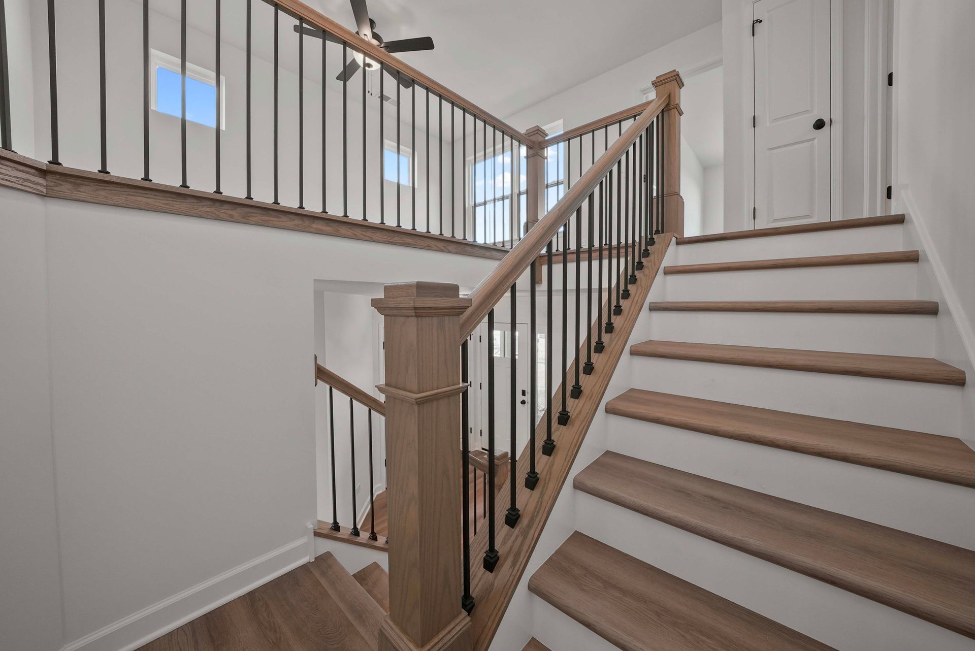 Bright hallway staircase with white walls, wood steps, and black metal railing by a landing.