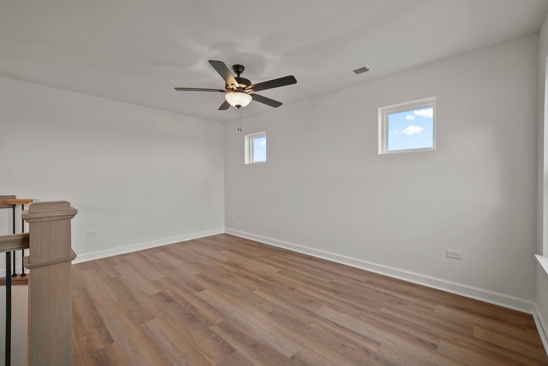 Empty white room with wood flooring, ceiling fan, and two small windows.