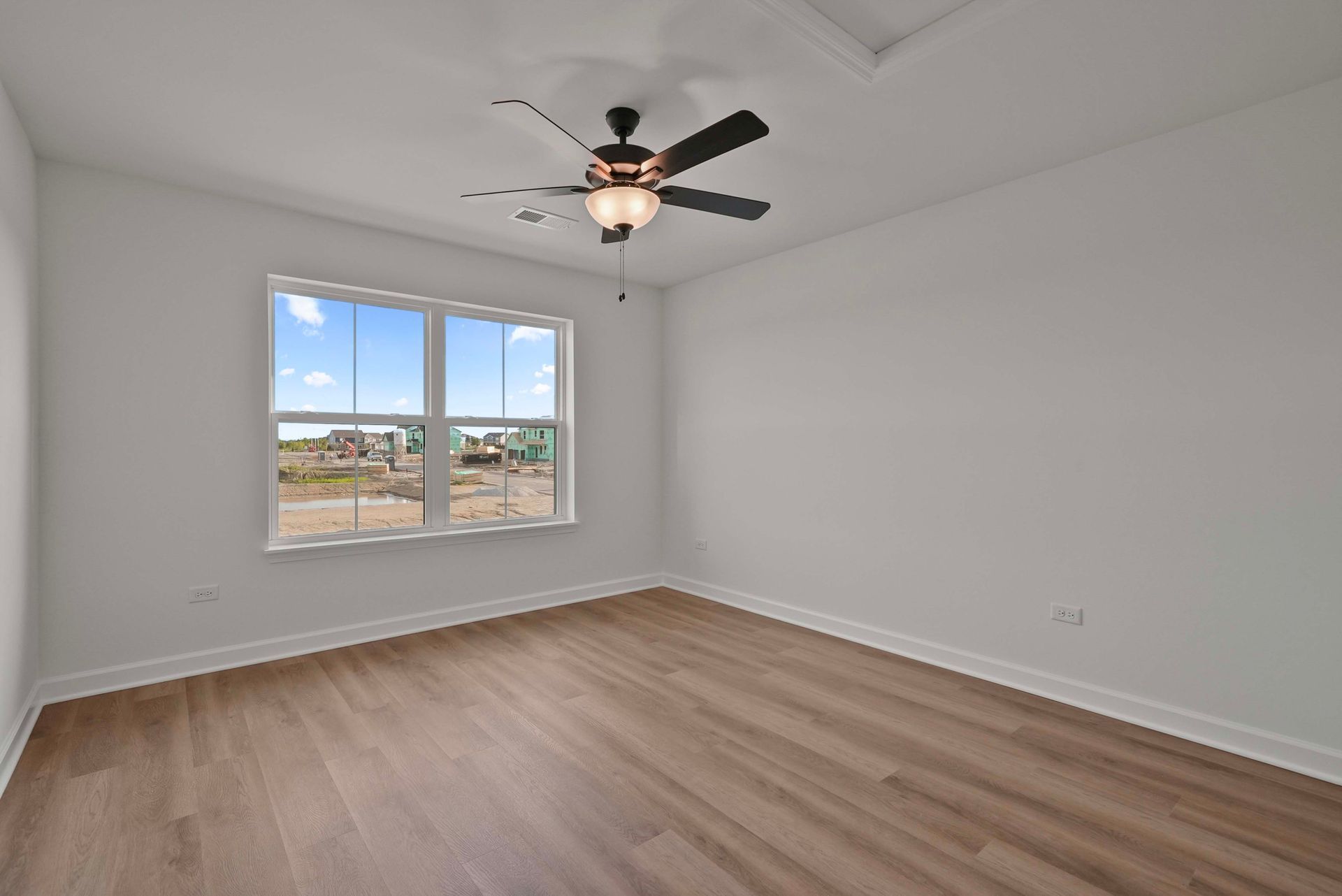 Empty white bedroom with wood-look floors, ceiling fan, and window view