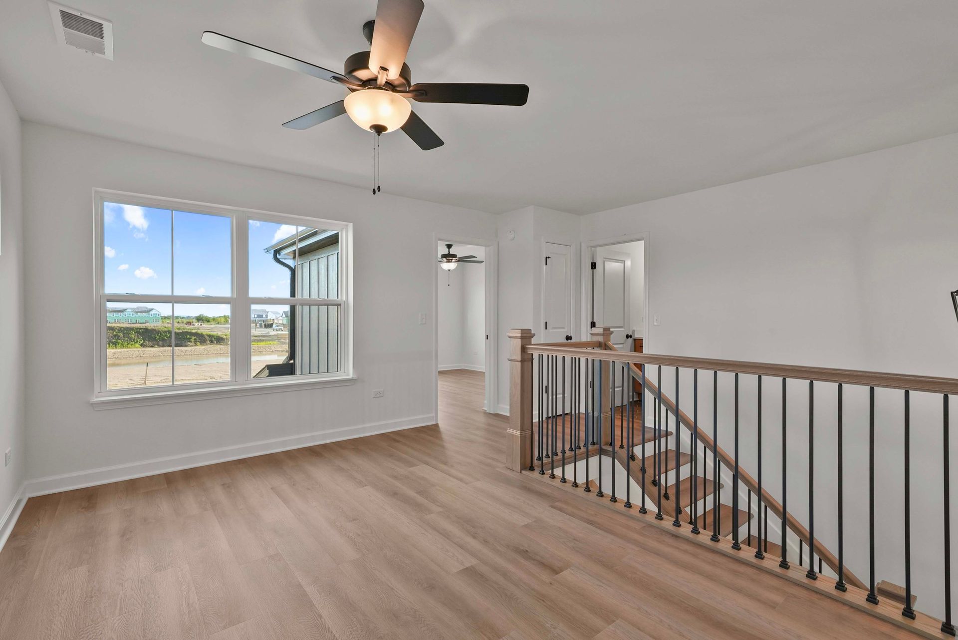 Bright upstairs hallway with wood floors, white walls, ceiling fan, and window overlooking open fields