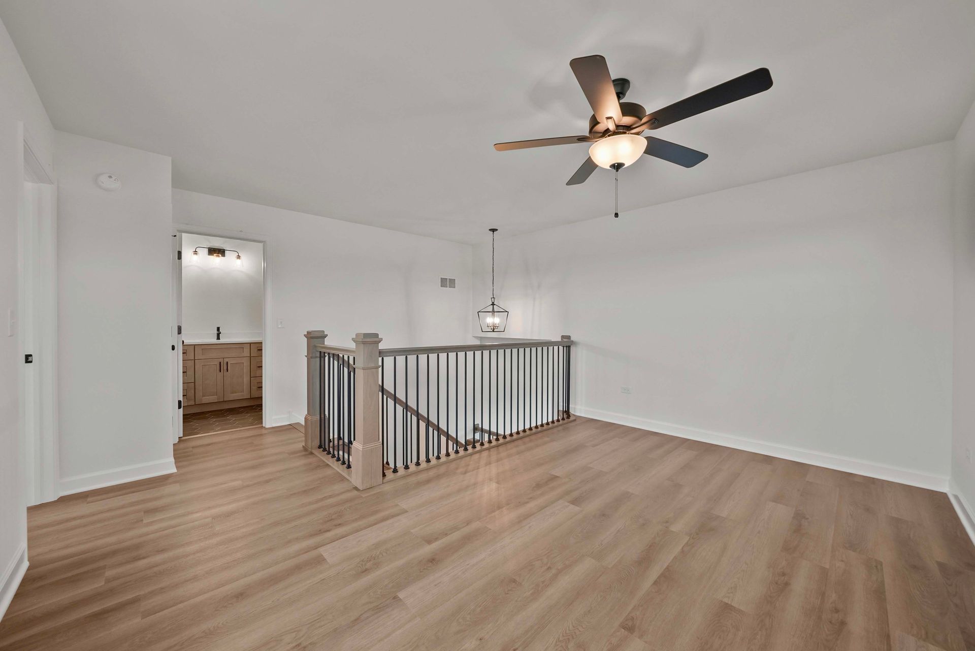 Spacious upstairs landing with wood floors, white walls, a ceiling fan, and a staircase railing overlooking below