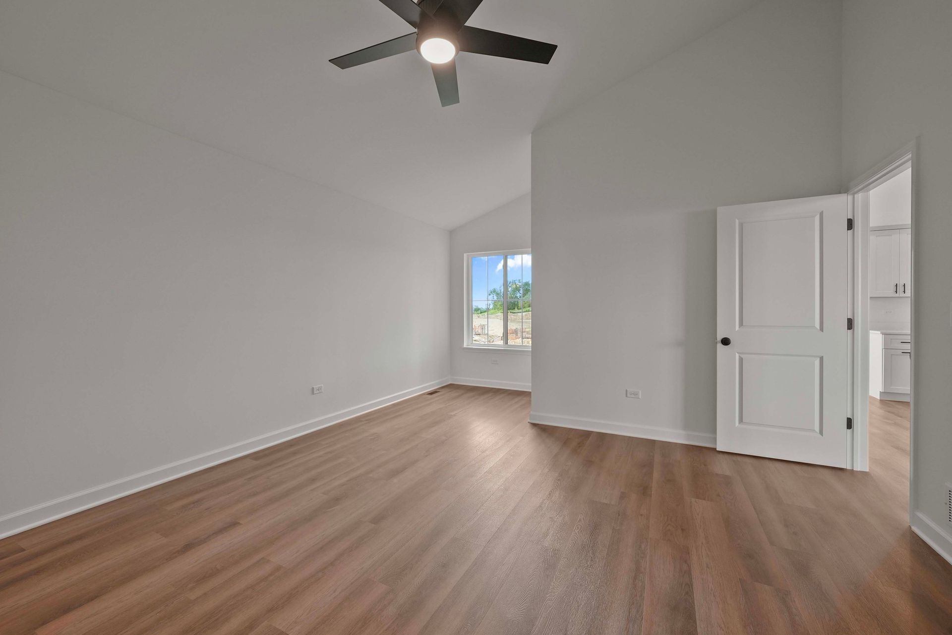 Empty white room with wood floors, ceiling fan, closet doors, and a bright window.