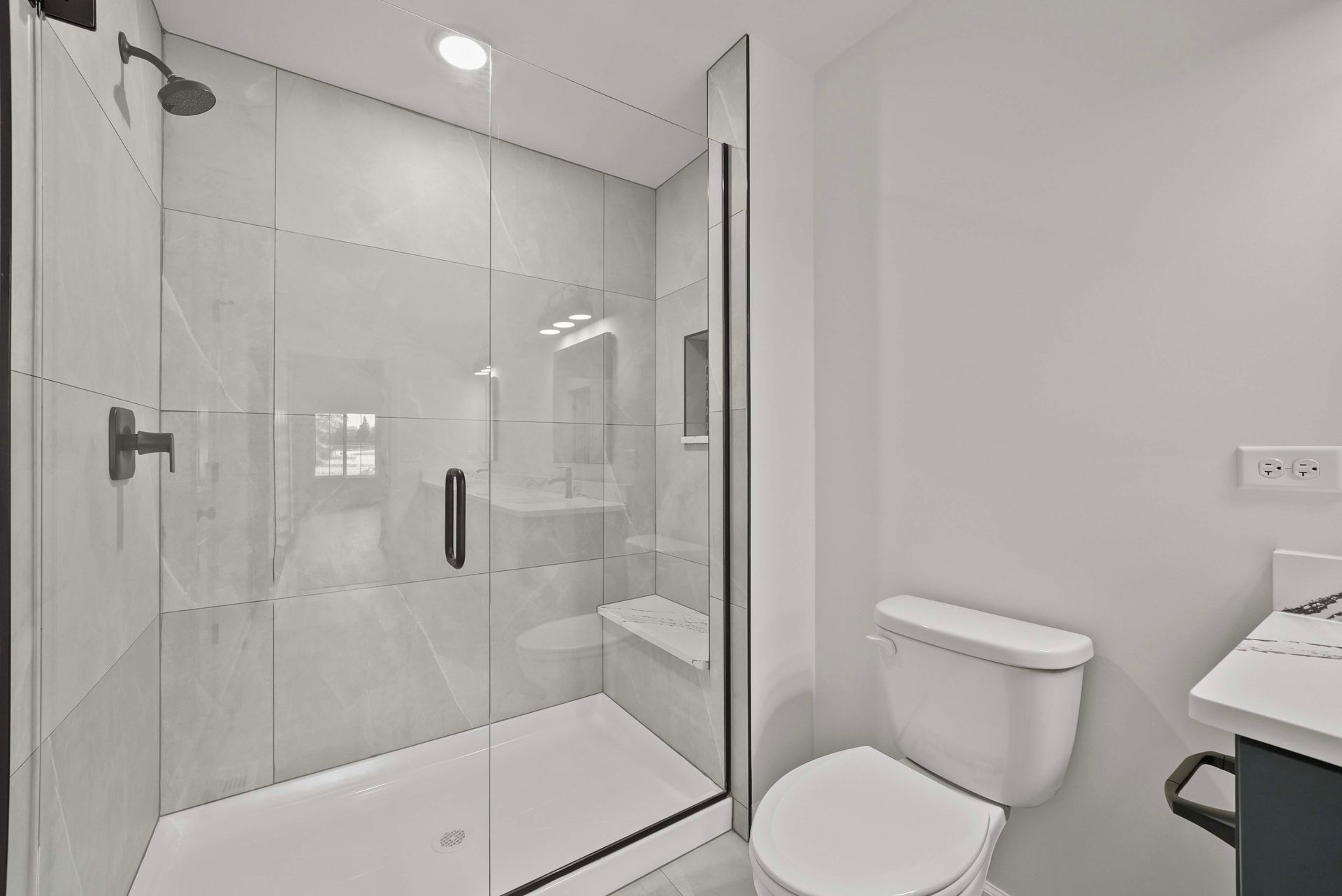 Modern white bathroom with glass shower enclosure, toilet, and vanity sink