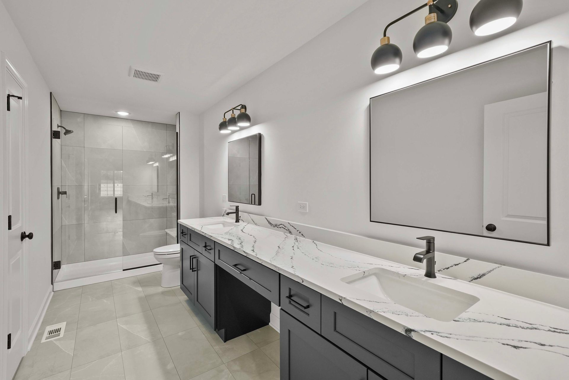 Modern bathroom with double vanity, large mirror, glass shower, and gray-and-white finishes