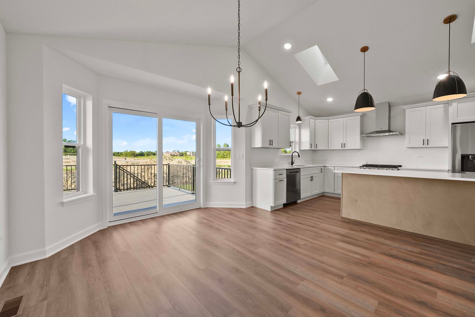 Bright open kitchen and dining area with white cabinets, wood floors, and sliding doors to a balcony