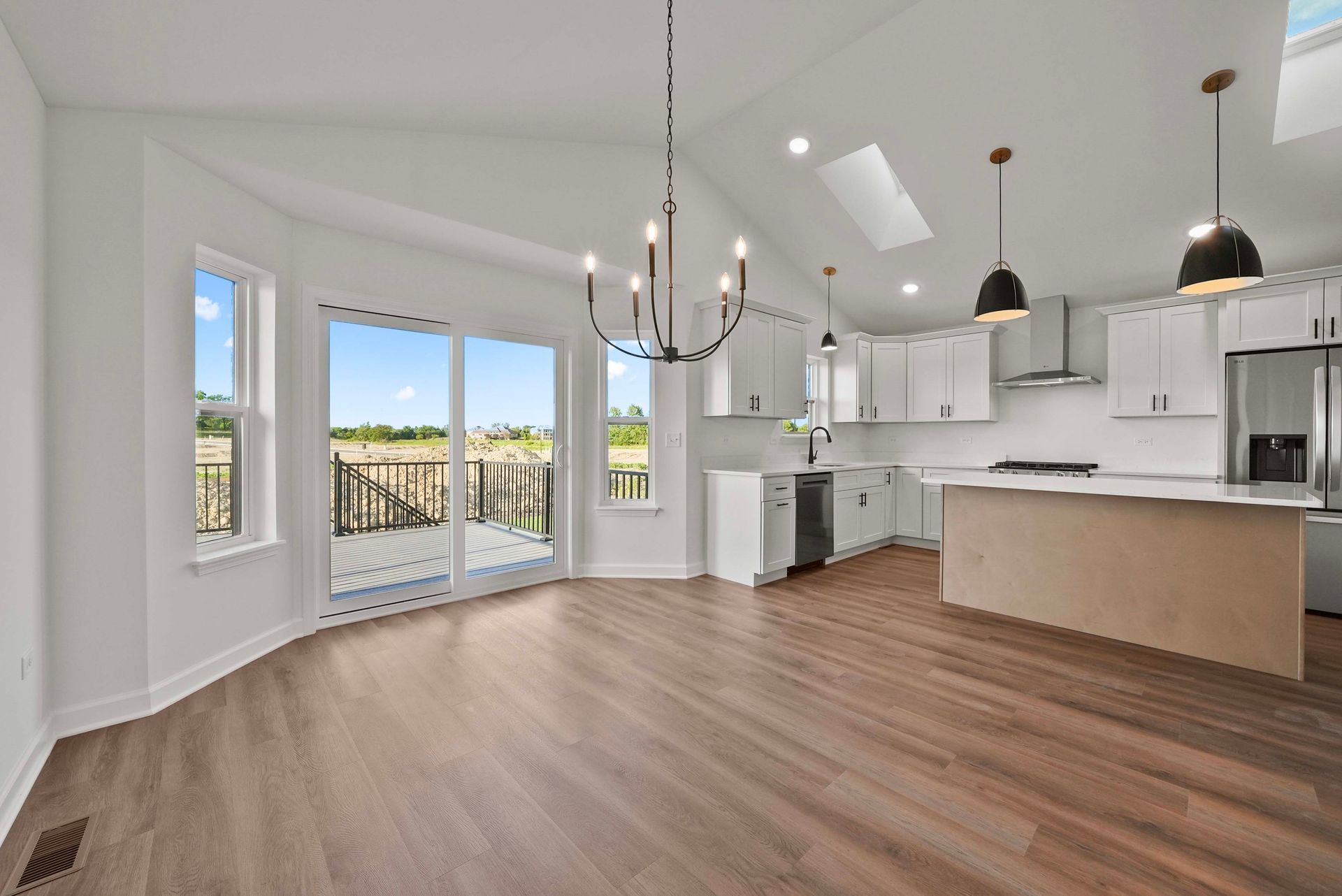 Bright open kitchen and dining area with white cabinets, island, wood floors, and balcony doors