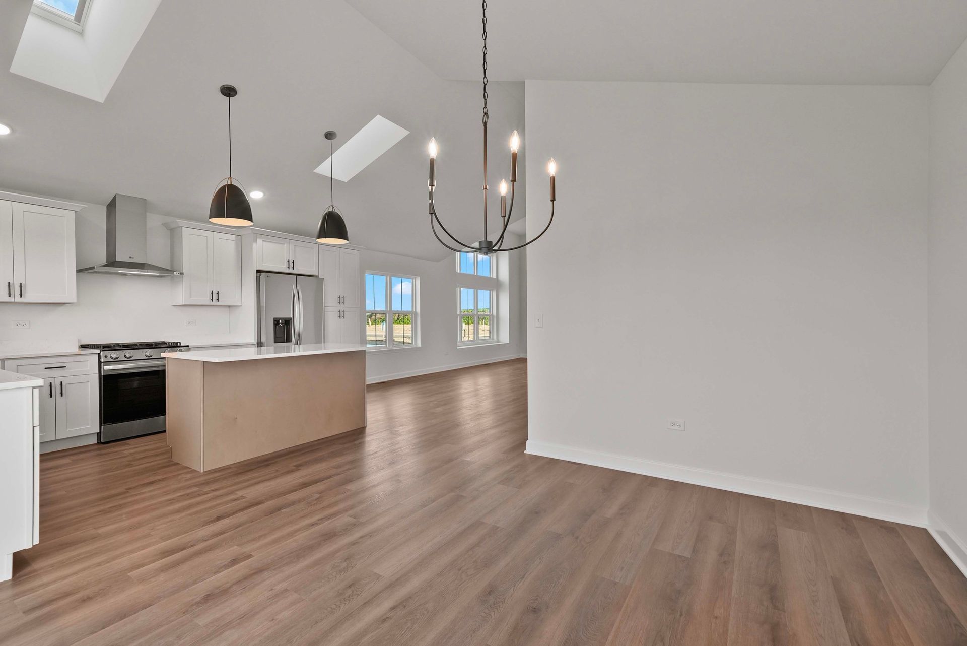 Bright open kitchen and dining area with white cabinets, wood floors, and a chandelier under vaulted ceilings