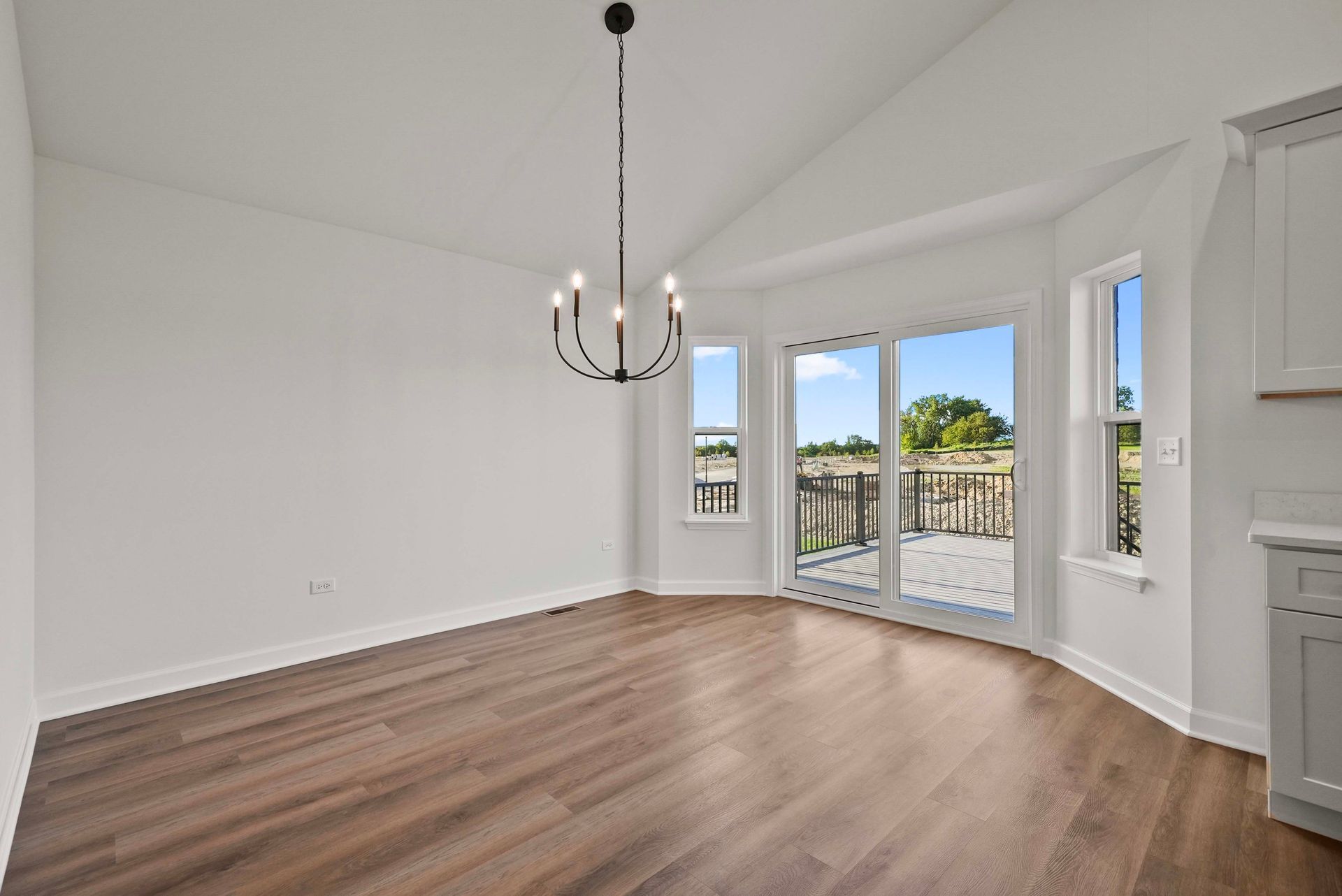 Empty bright room with white walls, wood floors, and bay windows overlooking a balcony