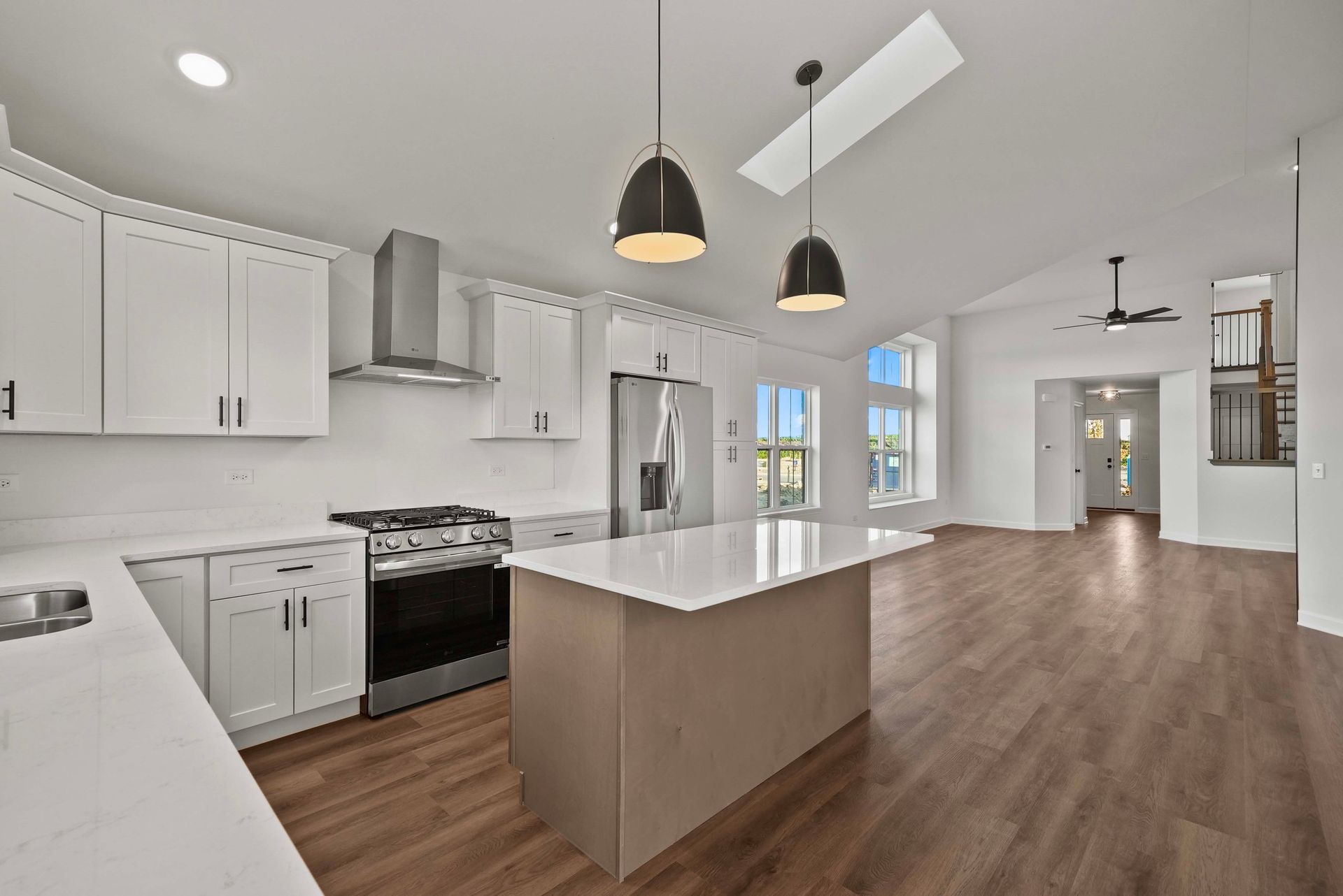Bright modern kitchen and open living area with white cabinets, island, pendant lights, and wood floors