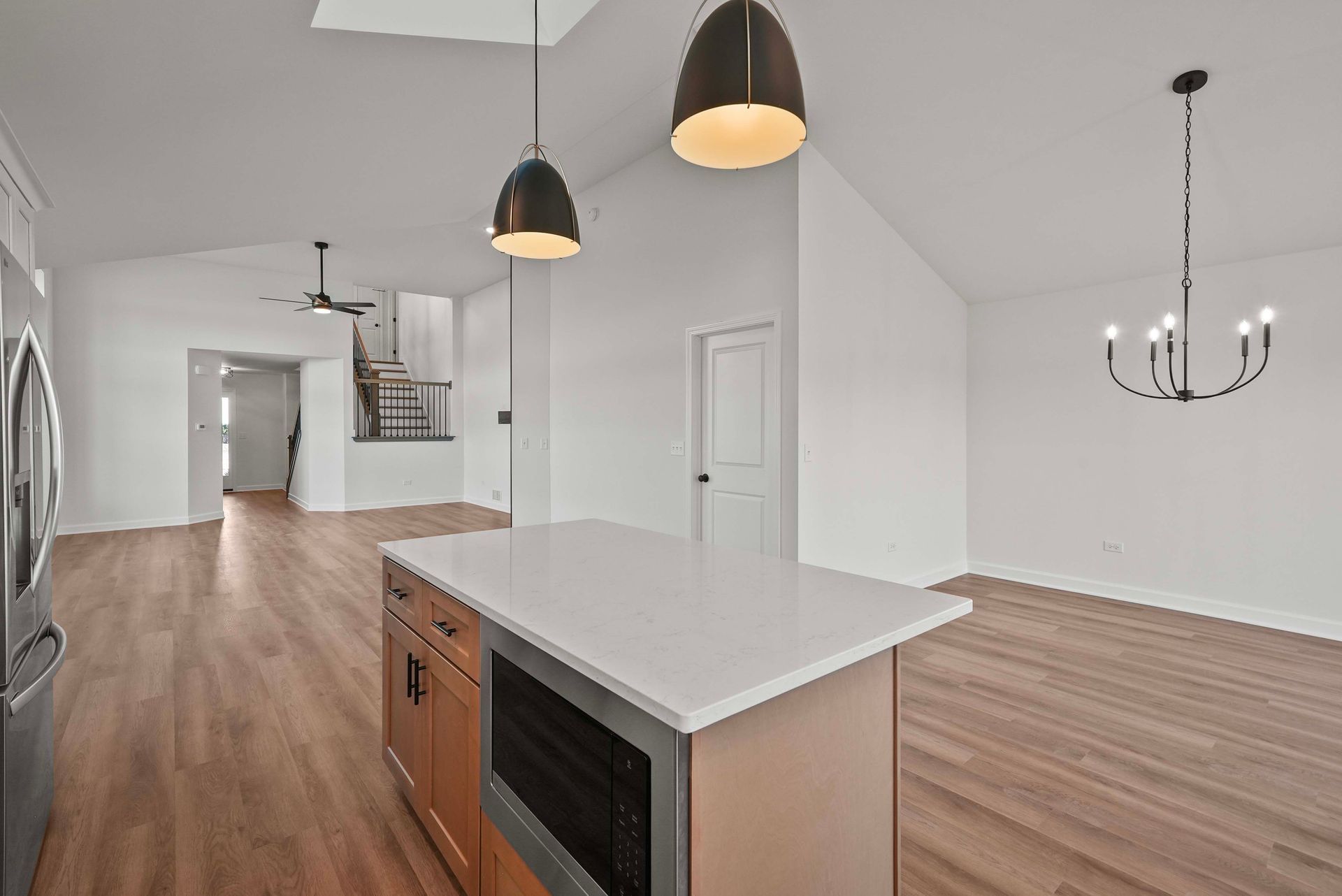 Bright open-concept kitchen and living room with wood floors, white walls, and pendant lights