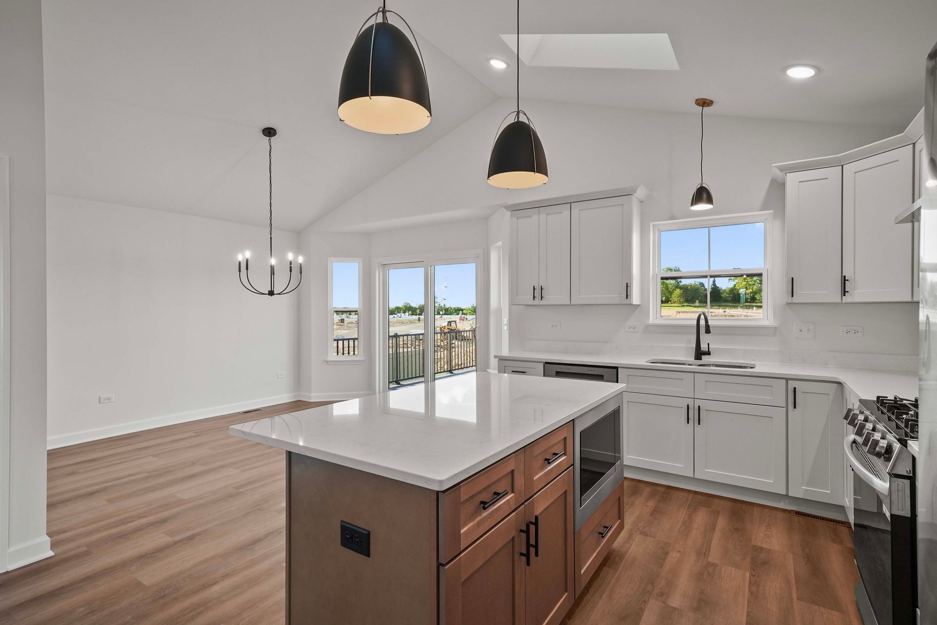 Bright modern kitchen with white cabinets, island, pendant lights, and wood floors opening to a dining area