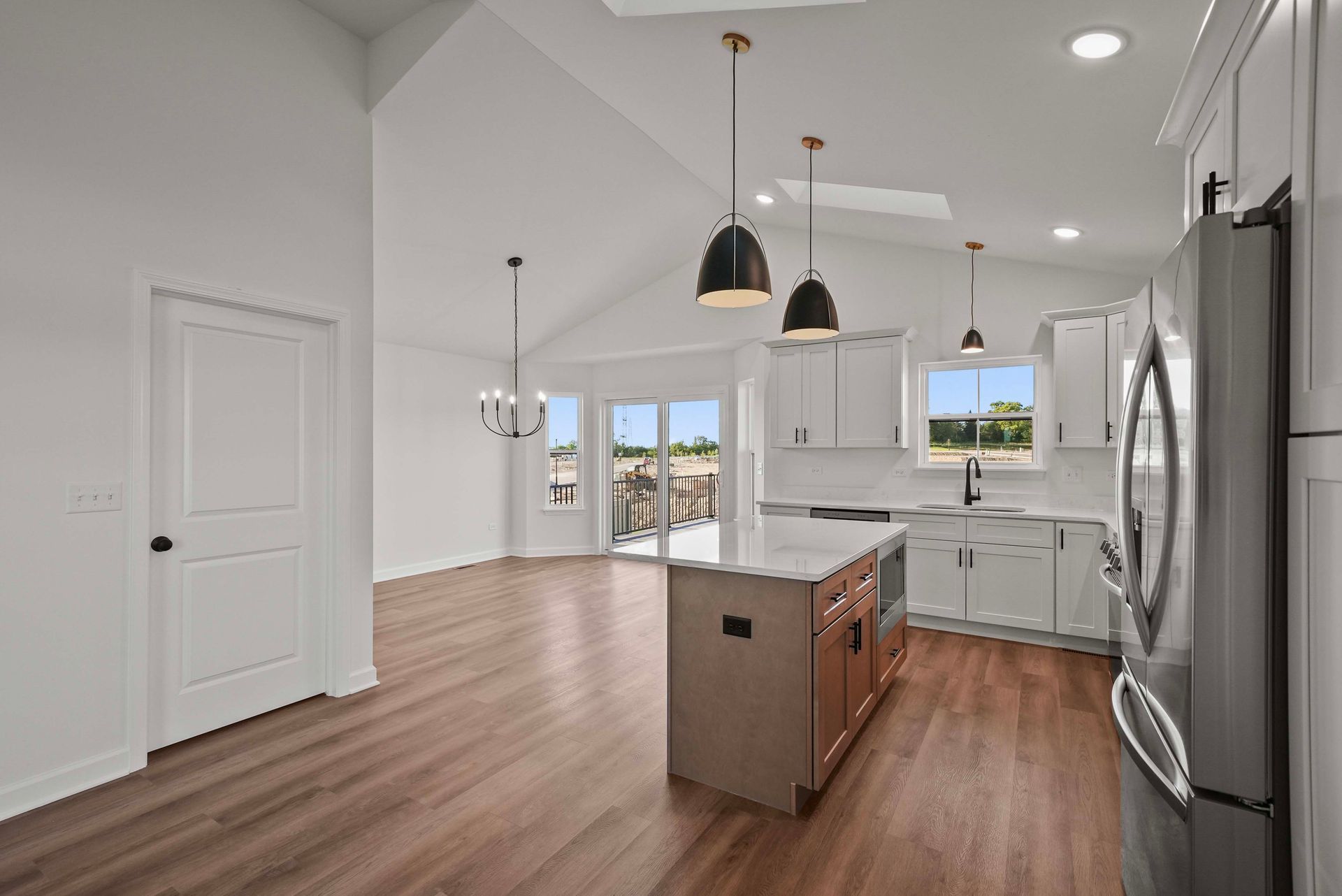 Bright modern kitchen with island, pendant lights, stainless fridge, and wood floors