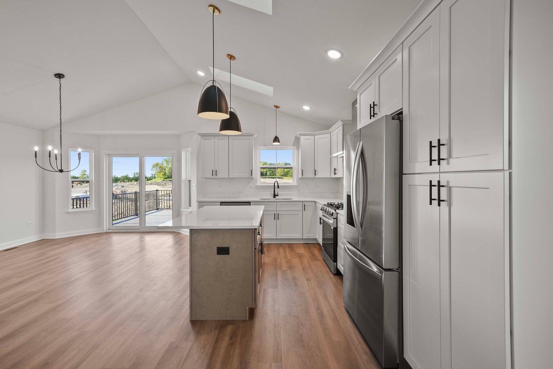 Bright modern kitchen with white cabinets, stainless appliances, island, and wood floors, opening to a dining area.