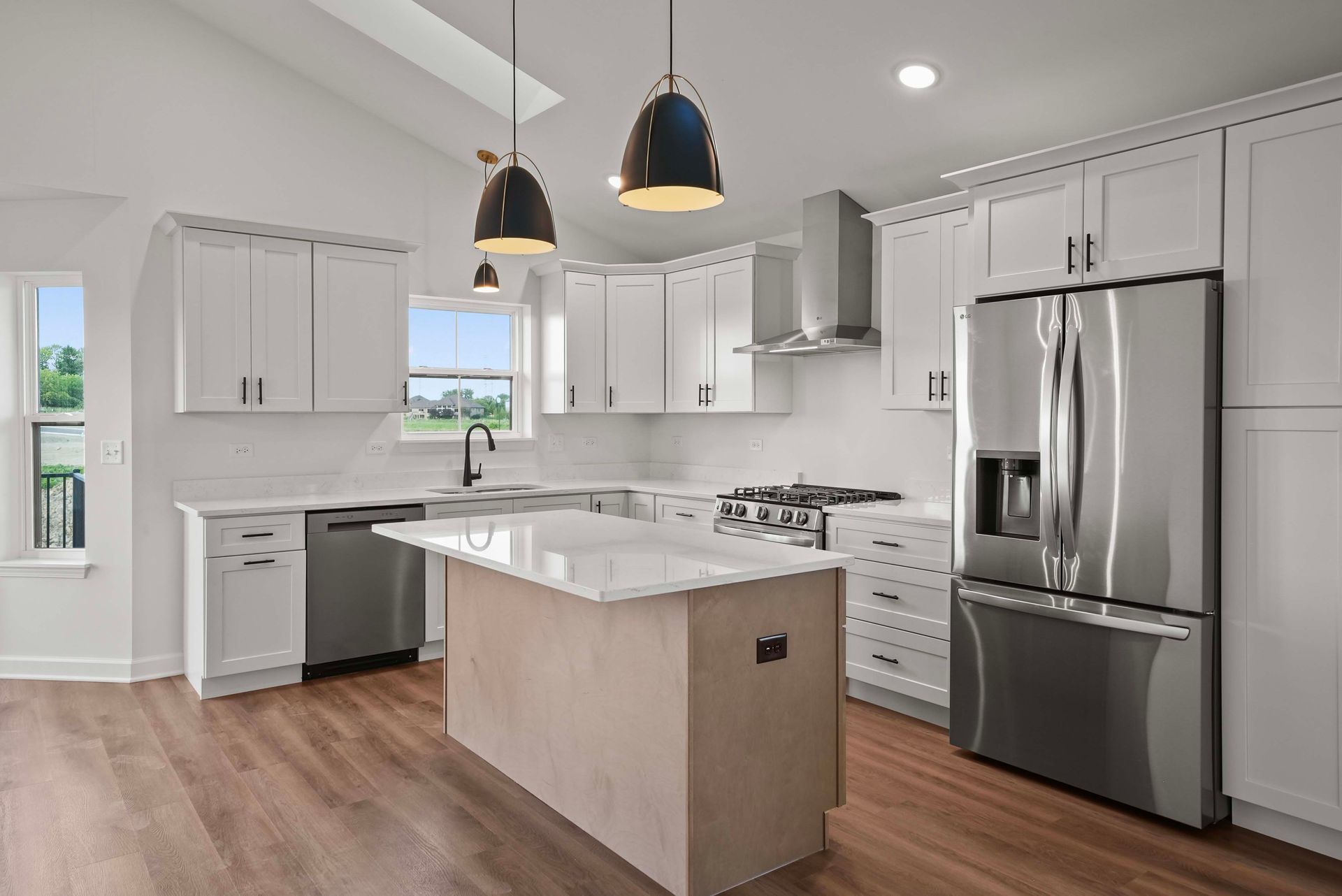 Modern white kitchen with island, stainless steel appliances, pendant lights, and wood flooring