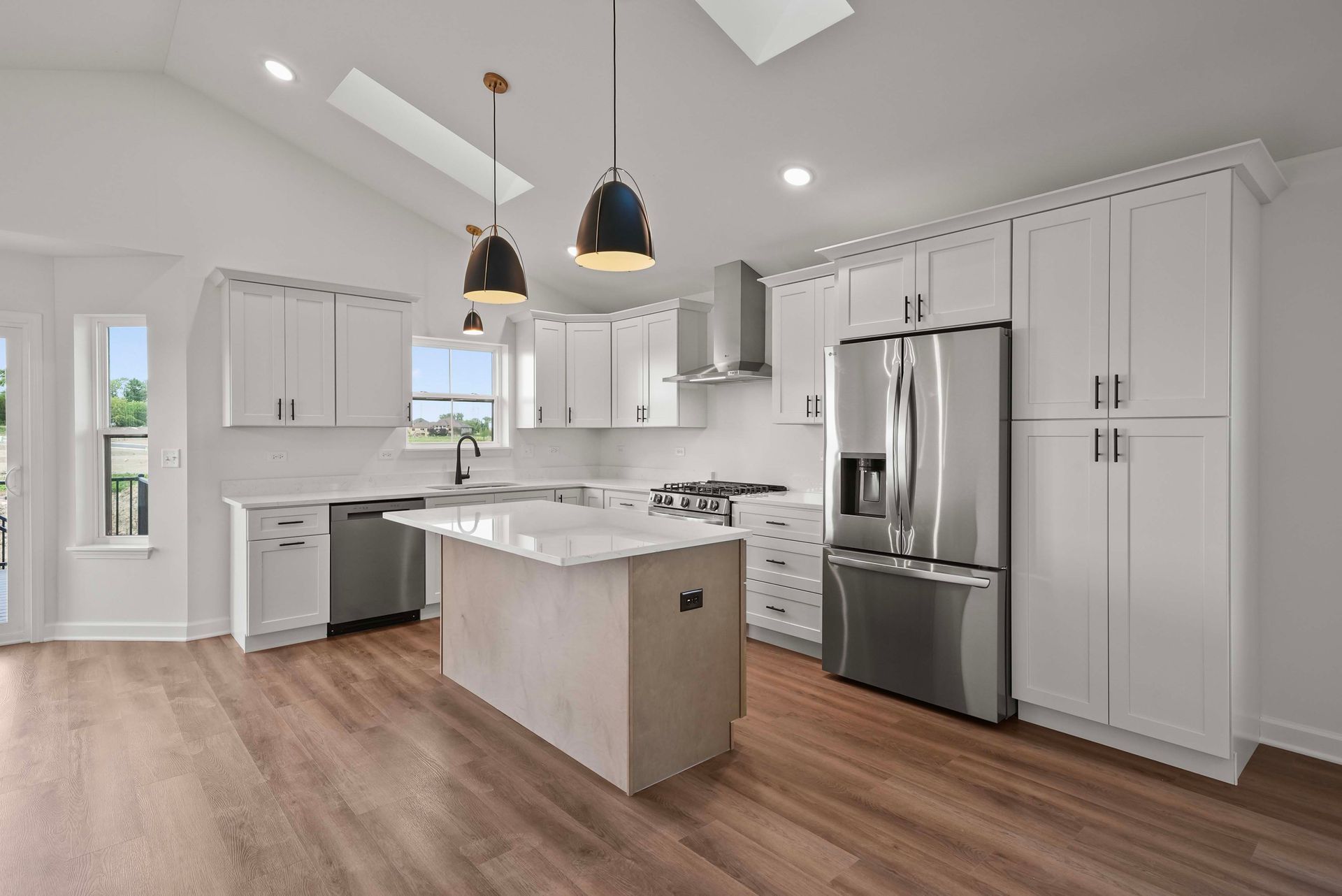 Bright modern kitchen with white cabinets, stainless steel appliances, island, and wood flooring