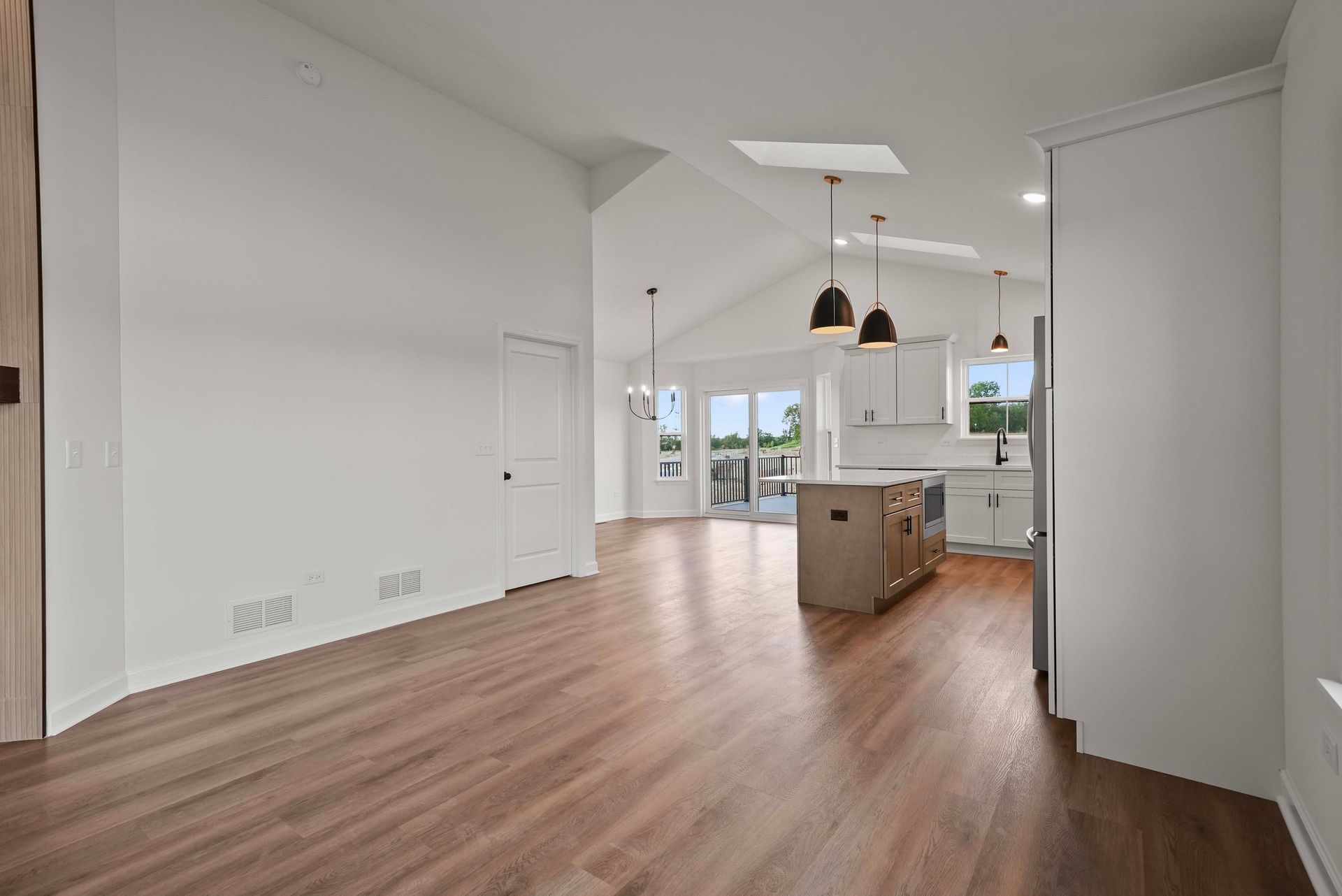 Bright open kitchen and living area with wood floors, island, pendant lights, and large windows