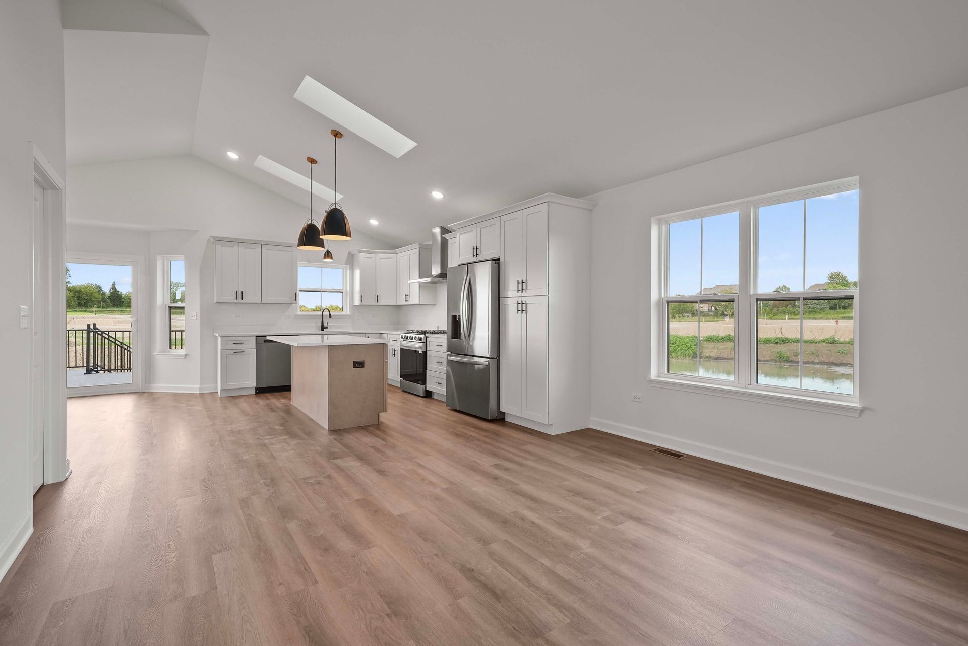 Bright open kitchen and living area with white cabinets, island, wood floors, and large windows