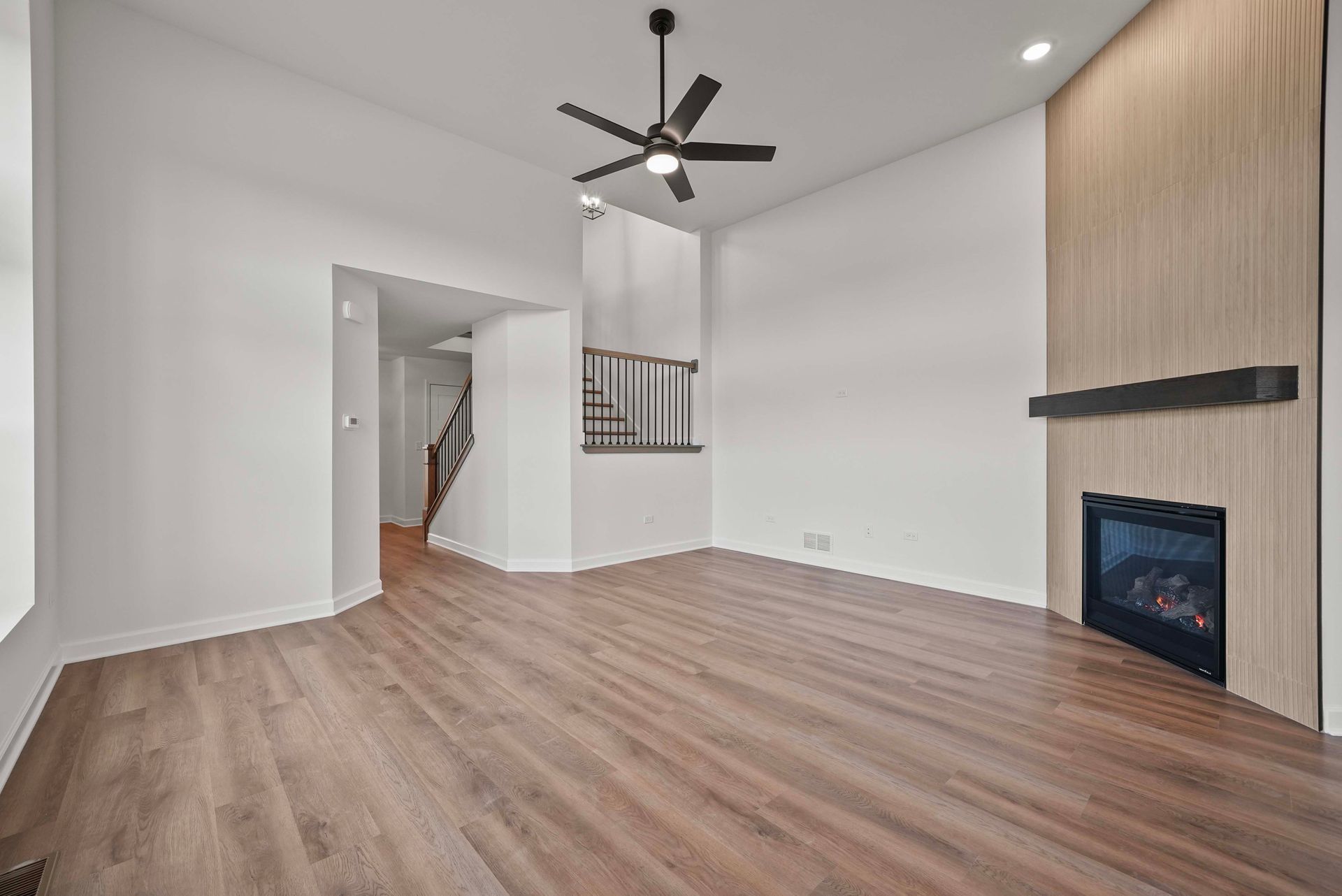 Spacious empty living room with wood floors, white walls, ceiling fan, and a modern fireplace.
