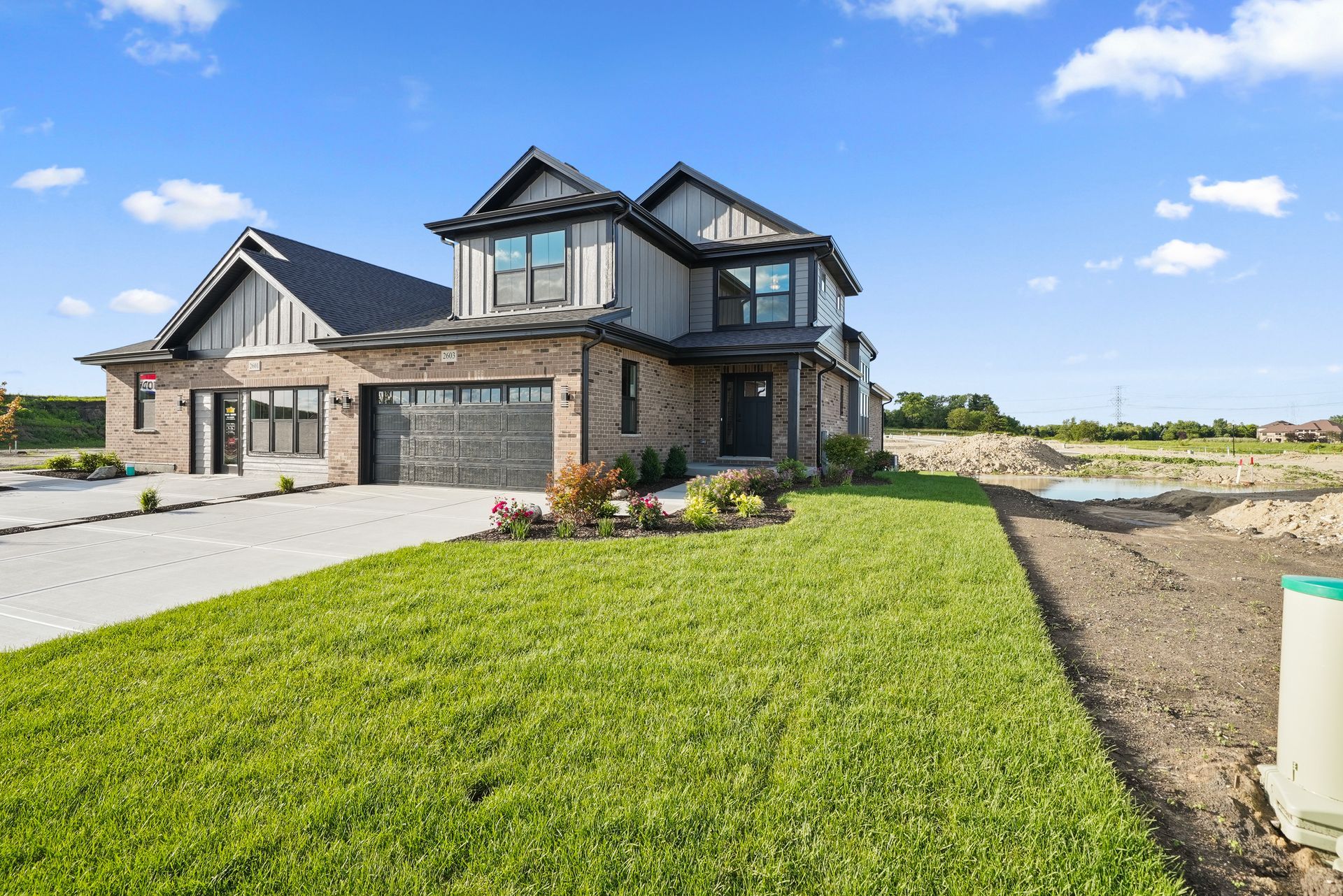 Modern two-story stone house with a green lawn and driveway under a blue sky
