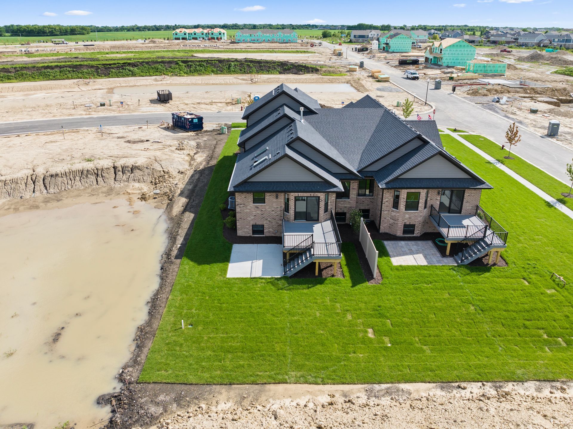 Modern black-roof house with stone facade beside muddy construction site and green lawn from above