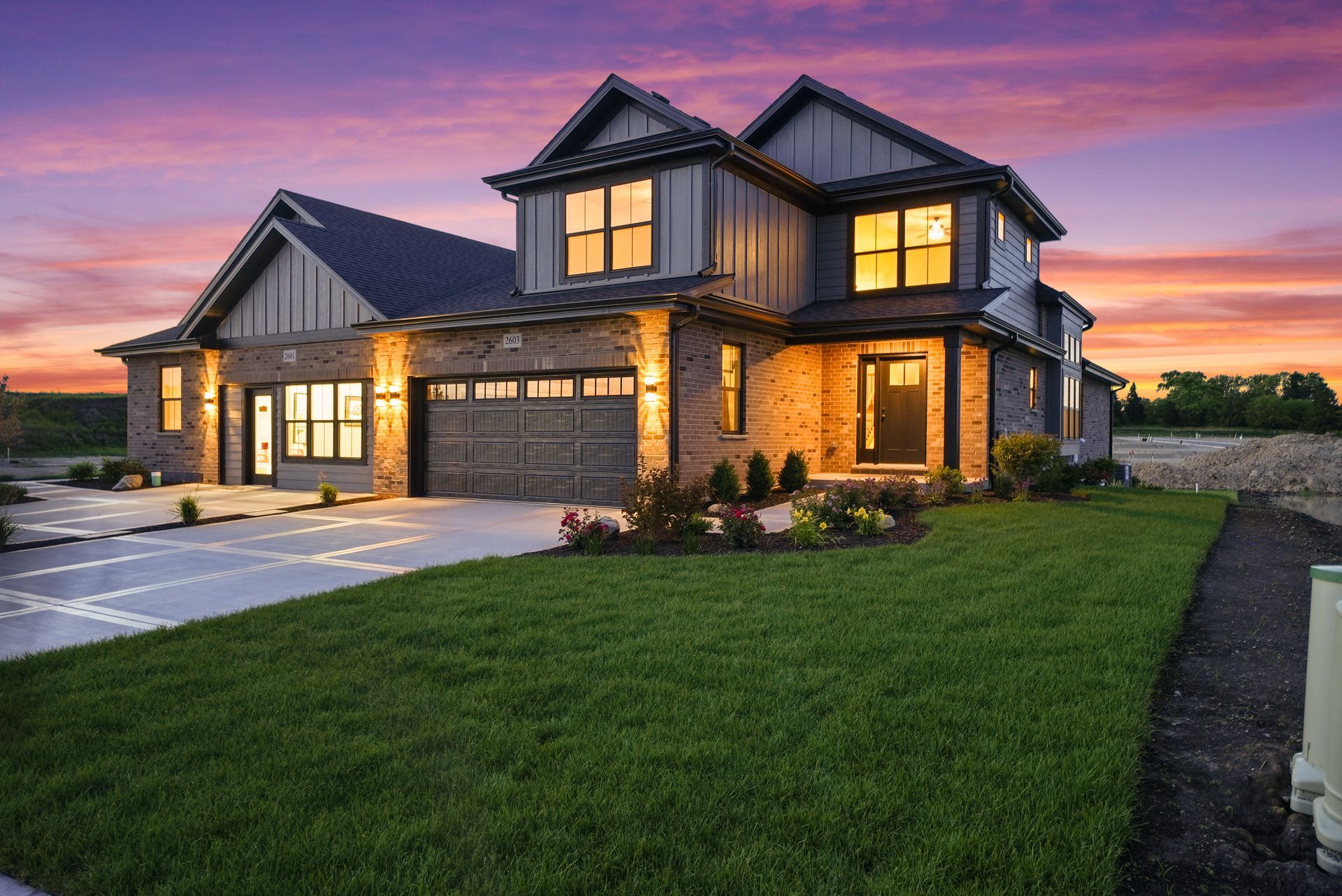 Modern two-story brick house with lit windows at dusk and a landscaped lawn