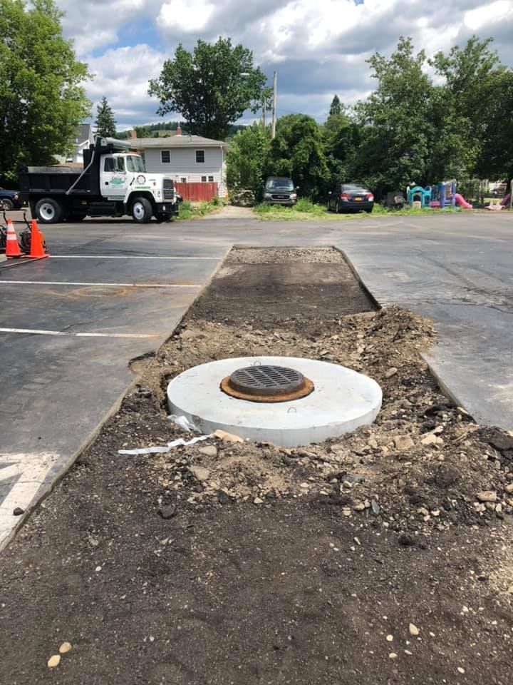 A dump truck is parked in a parking lot next to a manhole cover.