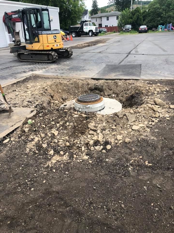 A yellow excavator is digging a hole in the ground in a parking lot.